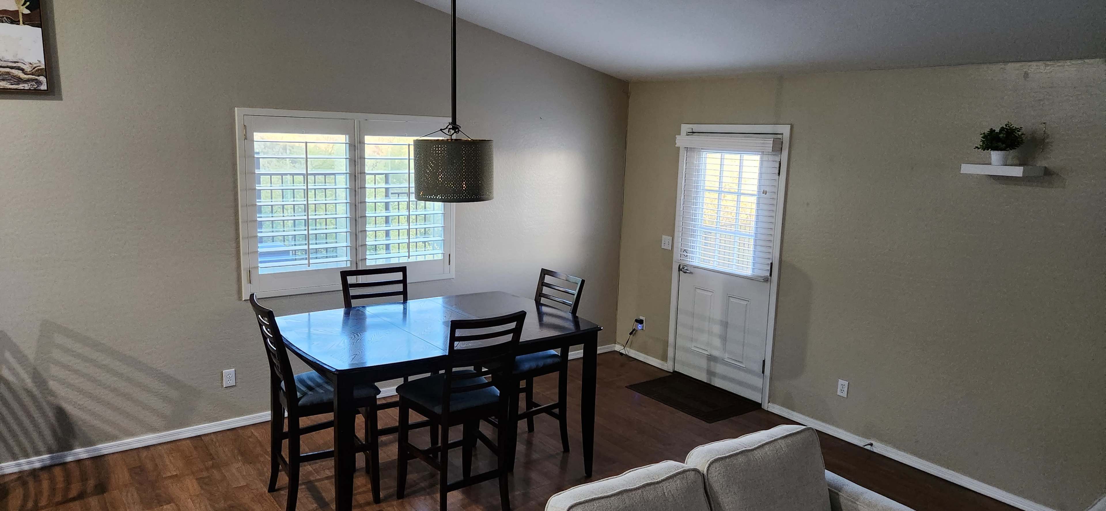 A dining area with a table and four chairs, a pendant light hanging above, and a door leading outside.