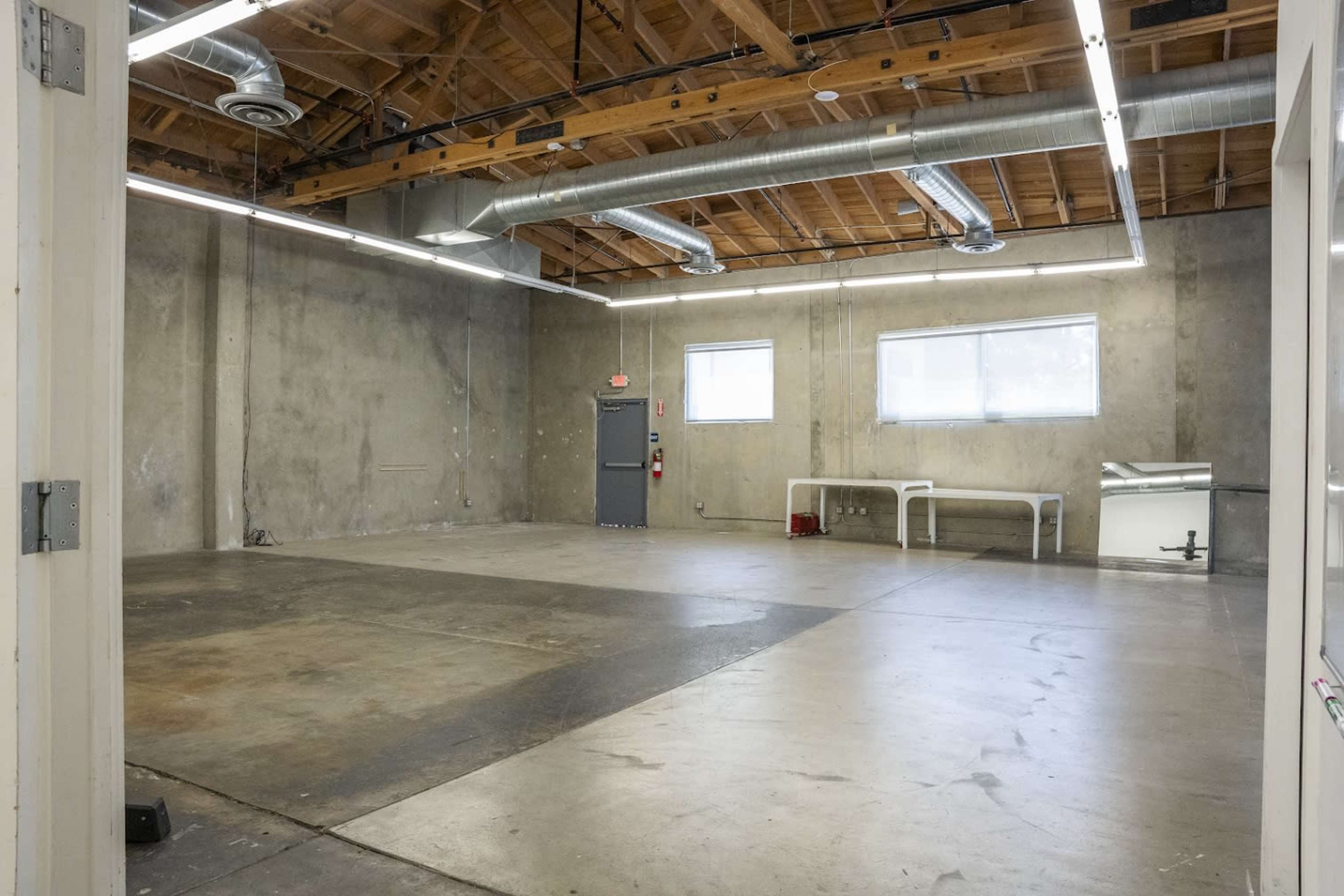 A spacious, empty room with concrete walls, a wooden ceiling, and large windows allowing natural light to enter.