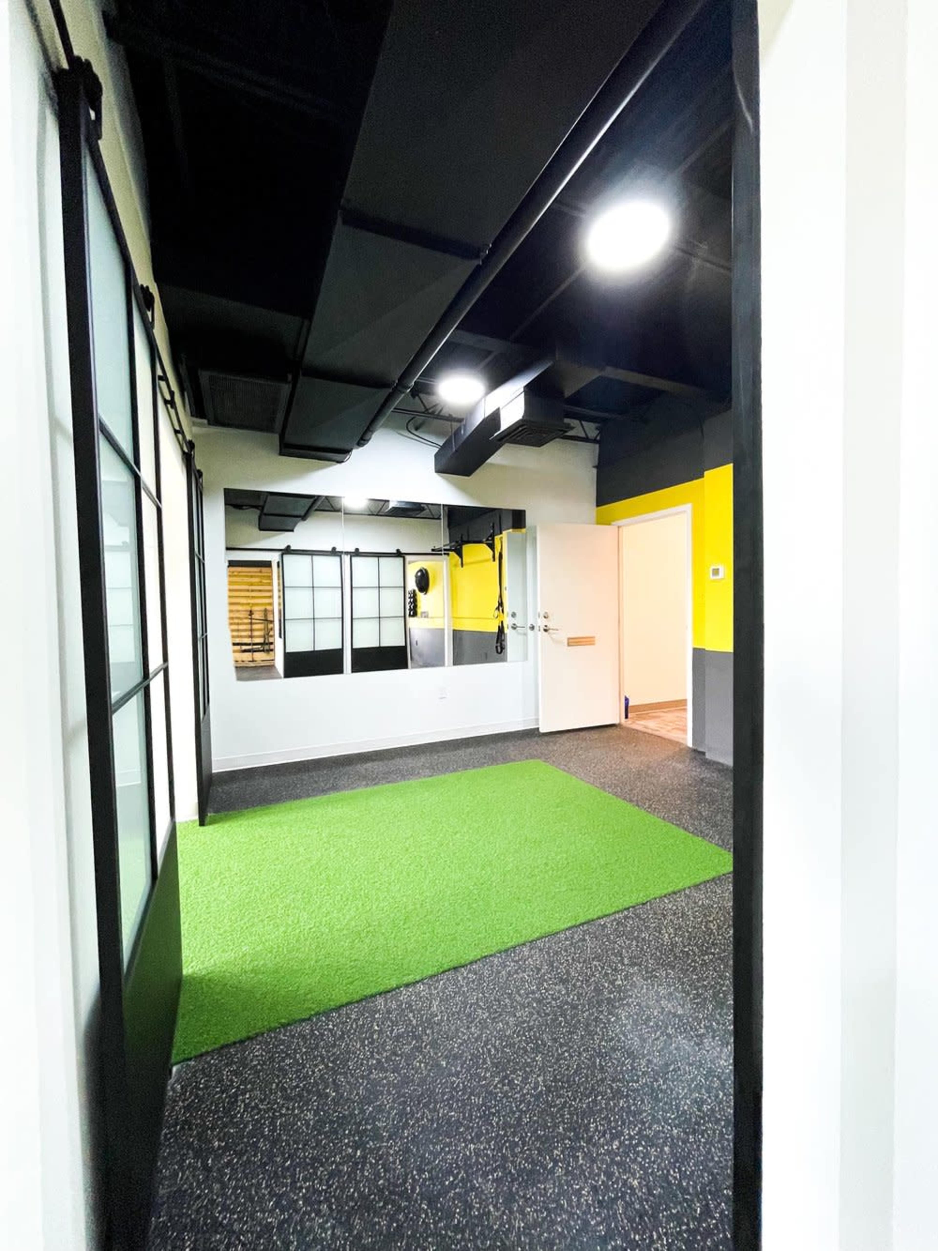 A fitness studio with green turf flooring, black and yellow walls, and large windows.