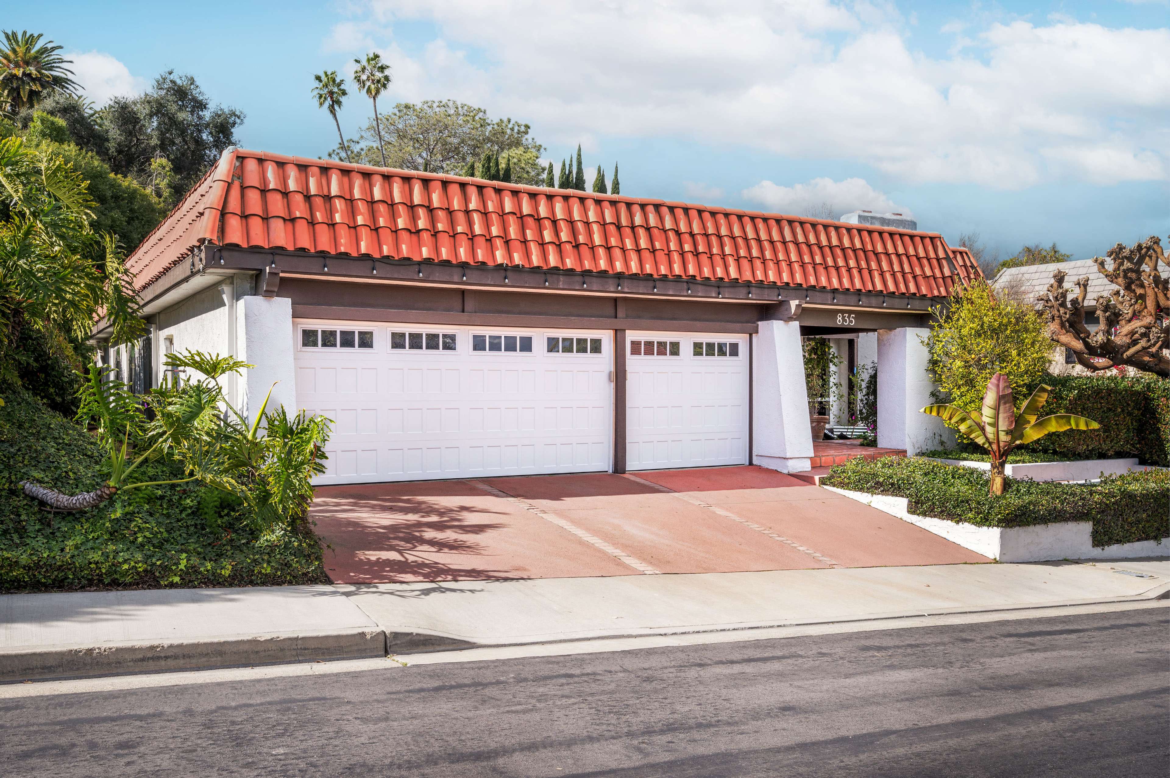A single-story house with a red tile roof and two garage doors is set on a landscaped lot.