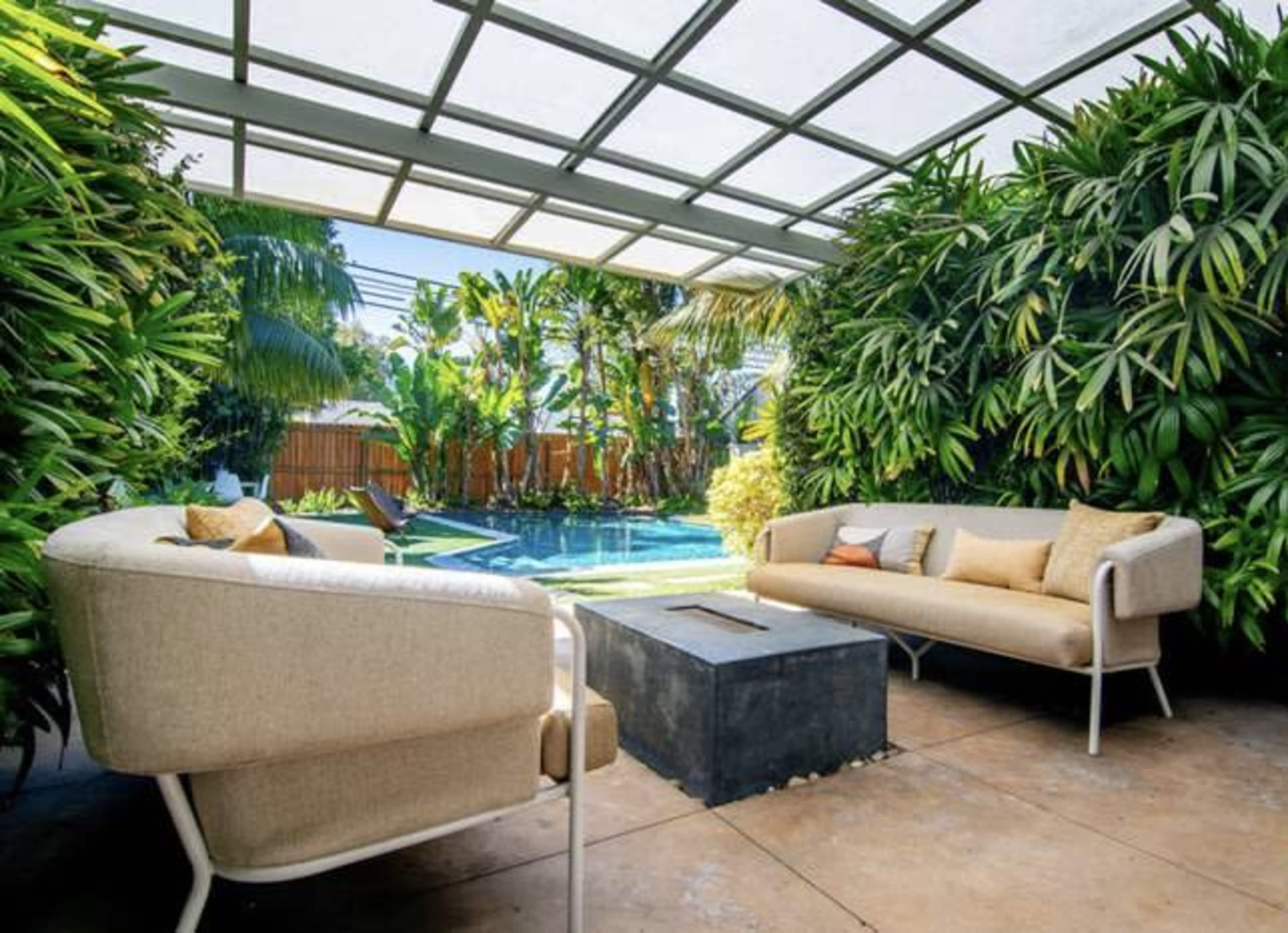A covered outdoor seating area features two chairs and a fire pit, overlooking a swimming pool surrounded by lush greenery.
