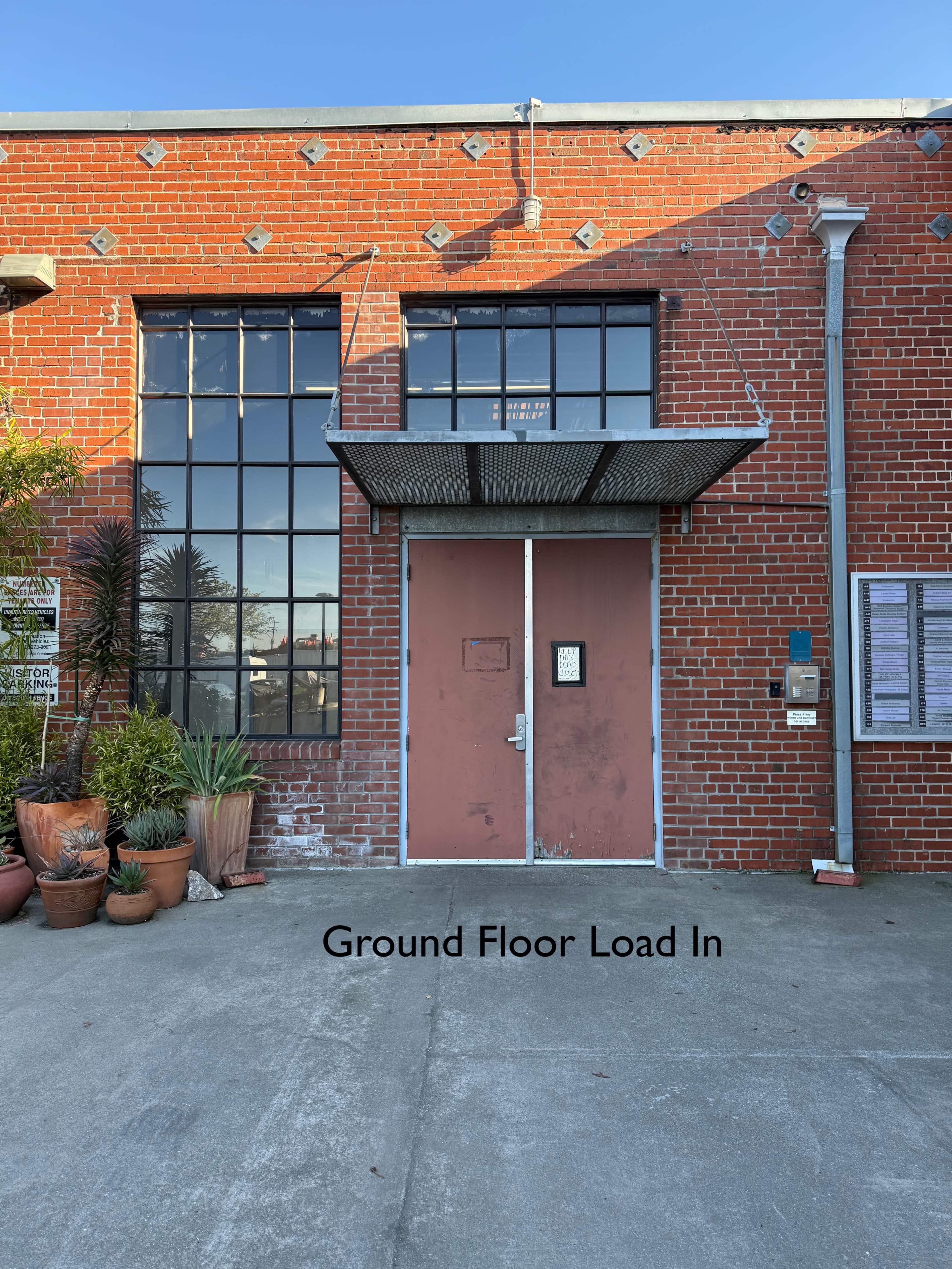 The image shows a brick building entrance with large windows and a canopy above double doors labeled "Ground Floor Load In."