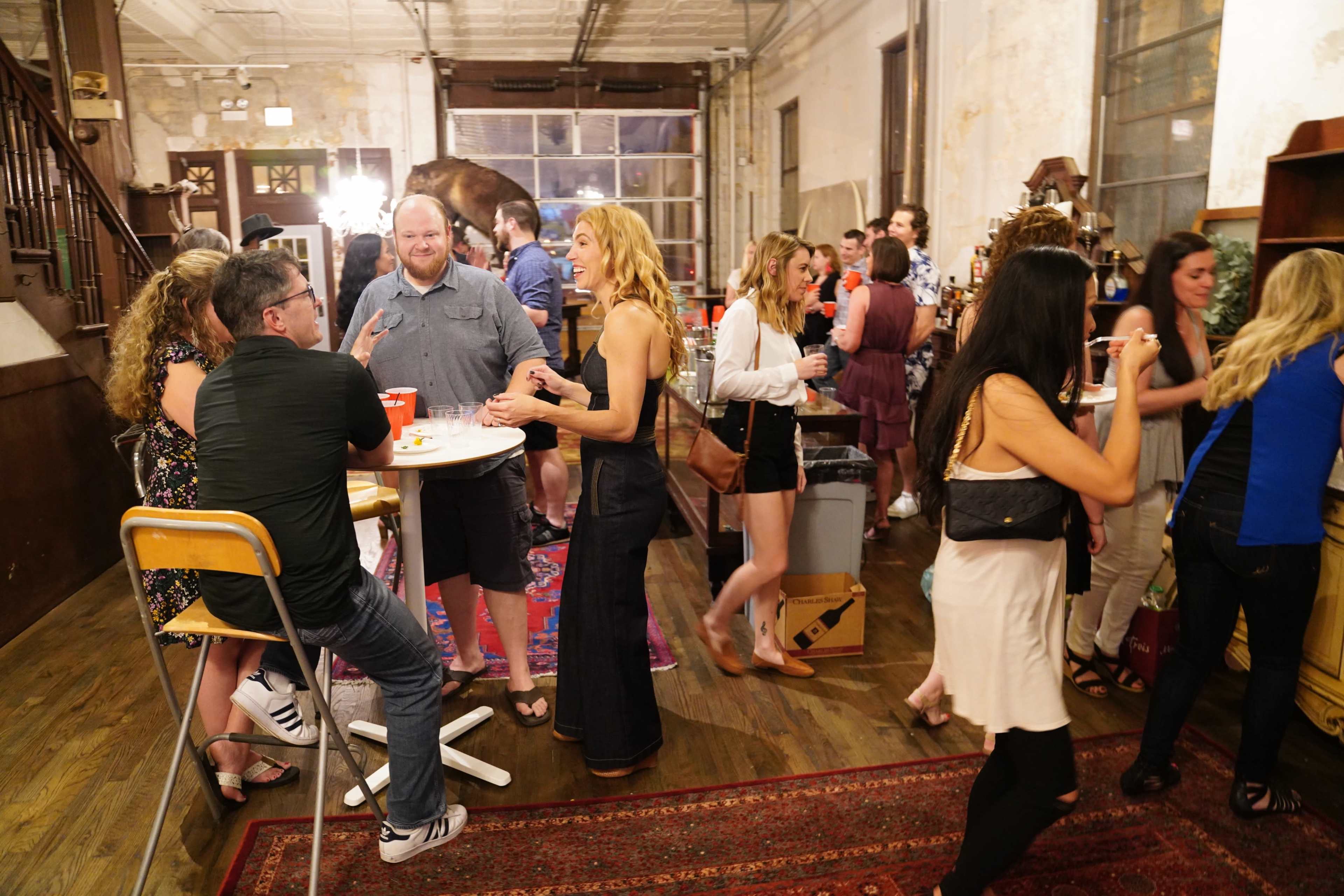 A group of people socialize at a lively gathering in an industrial-style venue.