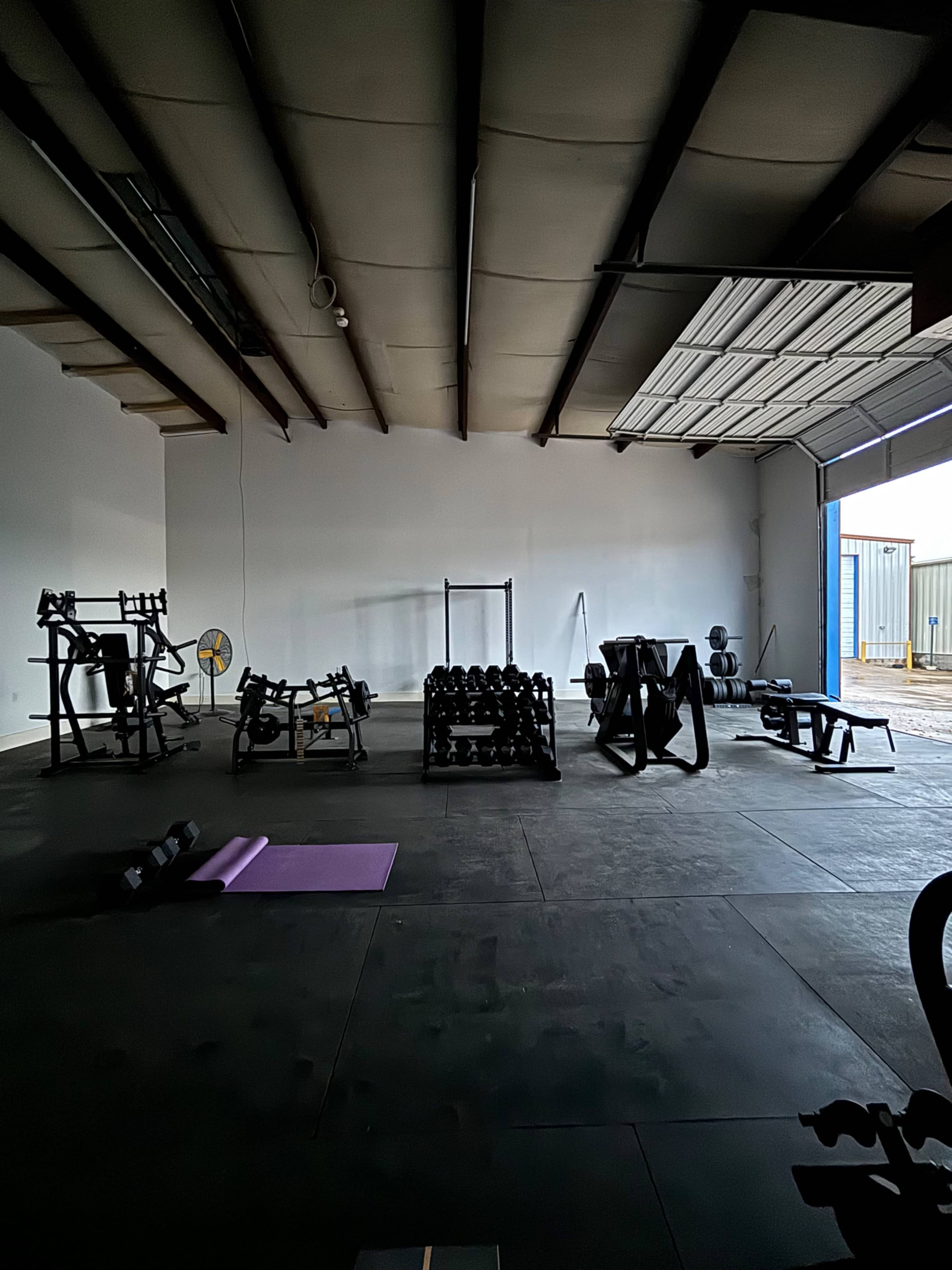 An empty gym interior with various fitness equipment, including dumbbells and weight machines, arranged around a spacious floor area.