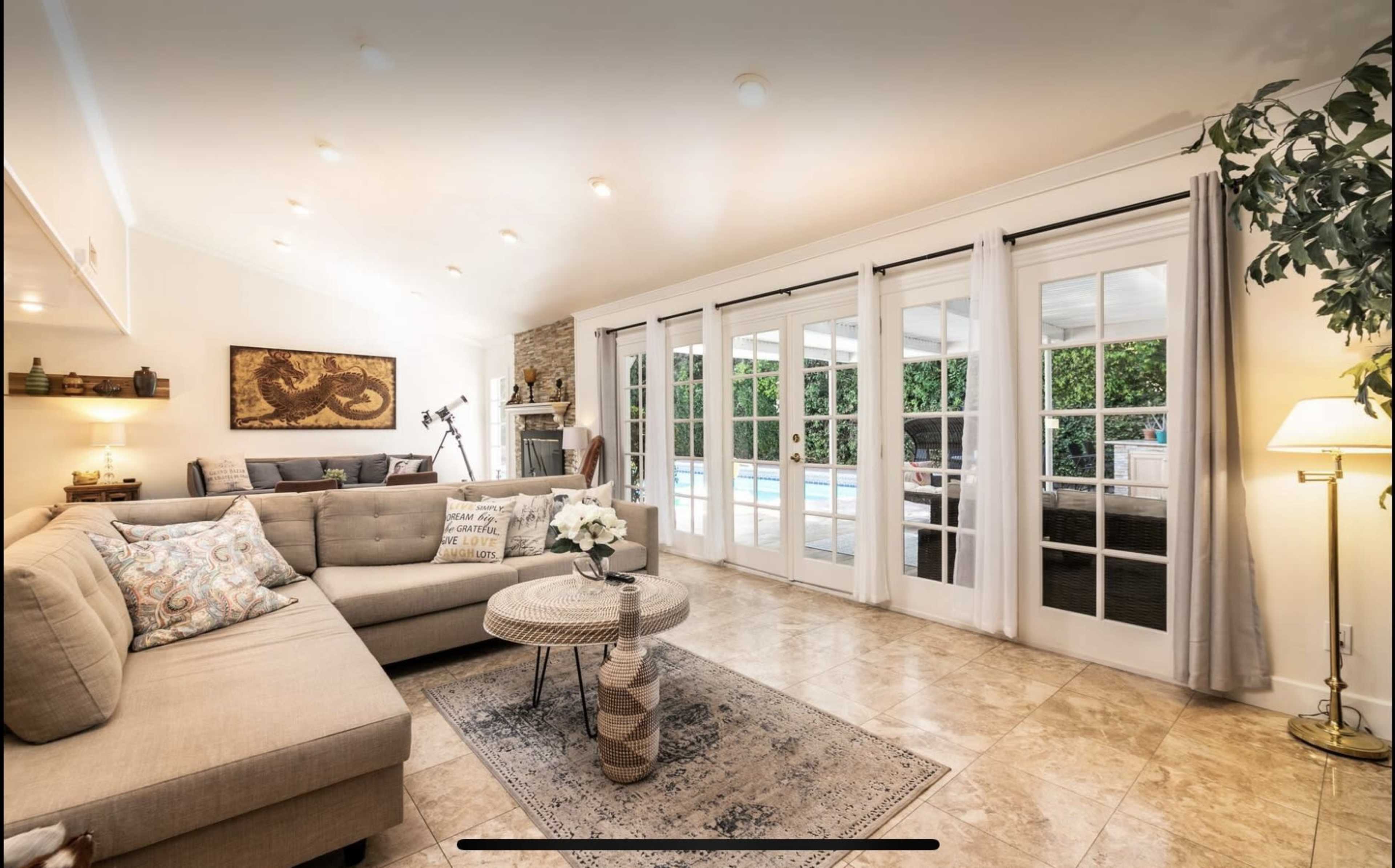 A bright living room with a sectional sofa, a round coffee table, and large glass doors leading to an outdoor pool area.