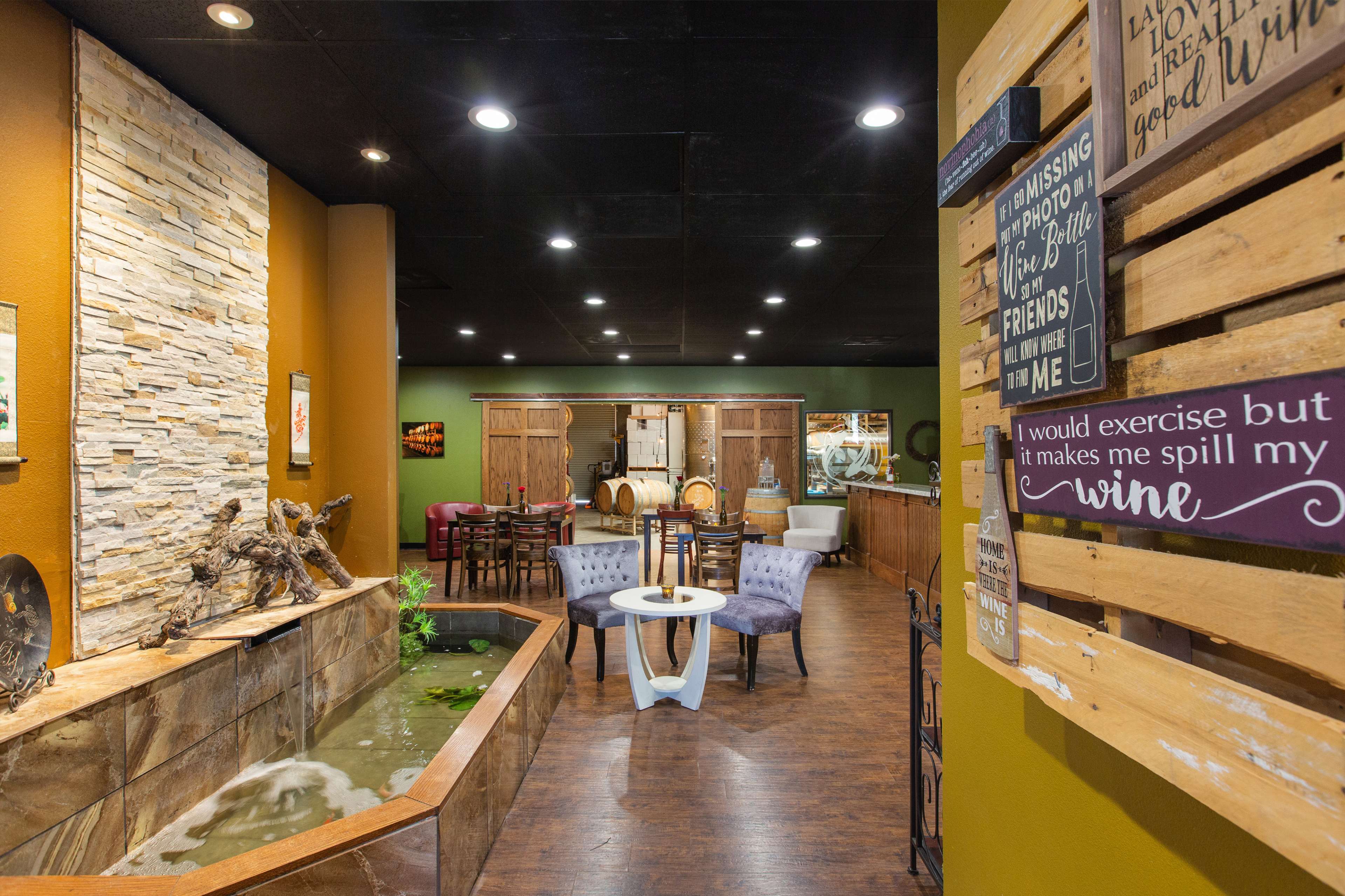 A cozy interior of a wine-themed establishment featuring stone walls, a small water feature, and seating areas with wooden decor.