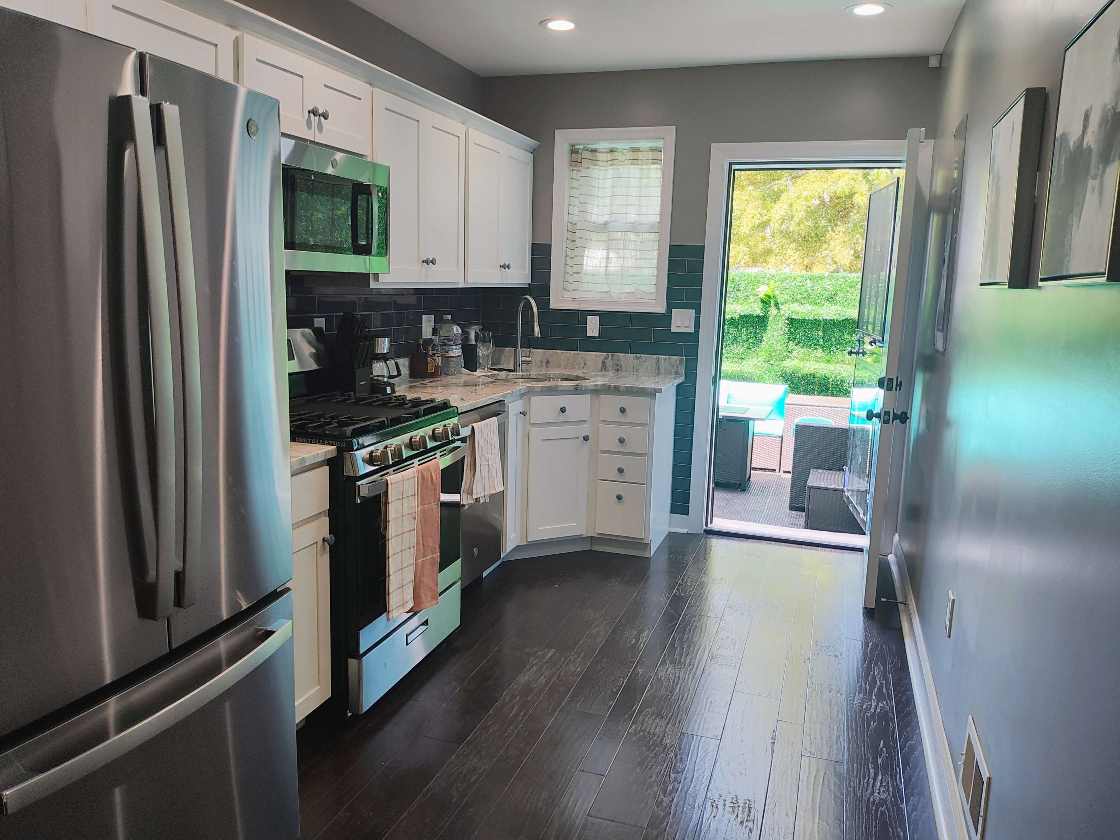 The image shows a modern kitchen with stainless steel appliances, white cabinets, and a door leading to an outdoor patio.