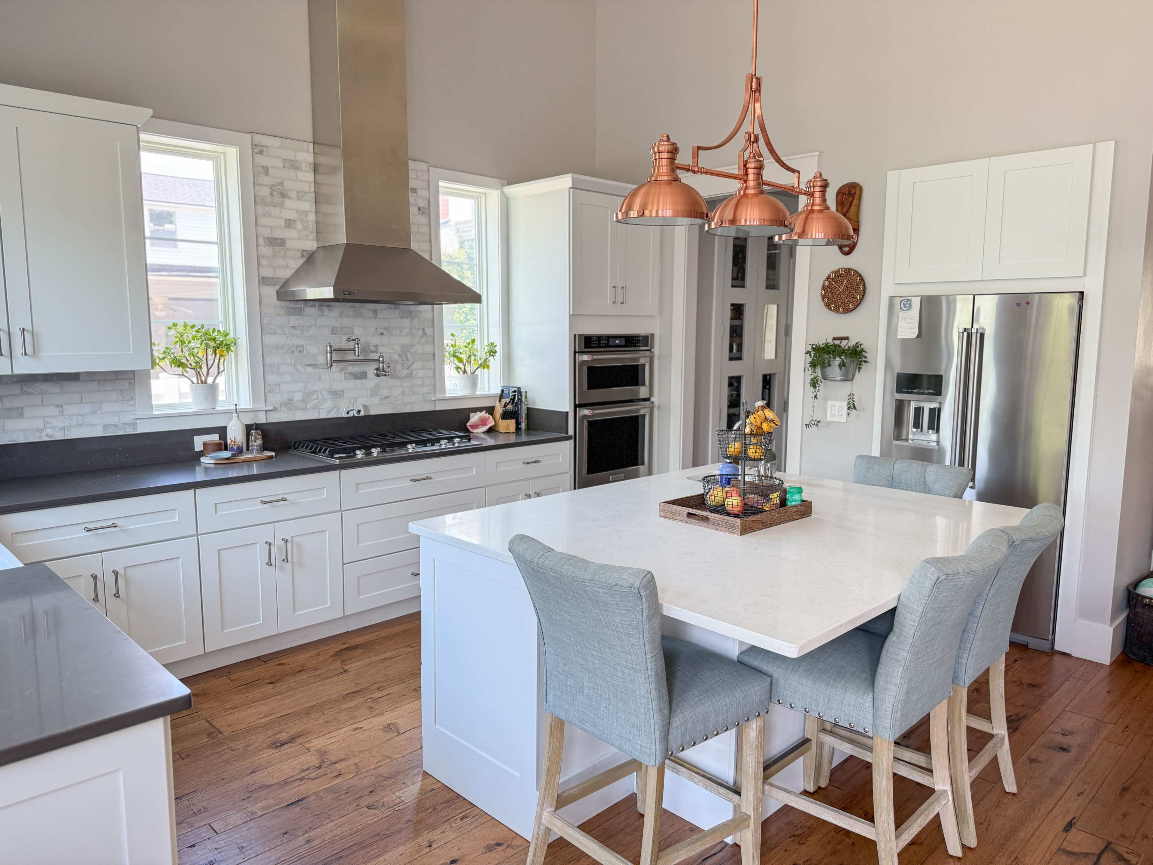 A modern kitchen features white cabinetry, a large island with a marble top, and copper pendant lights.