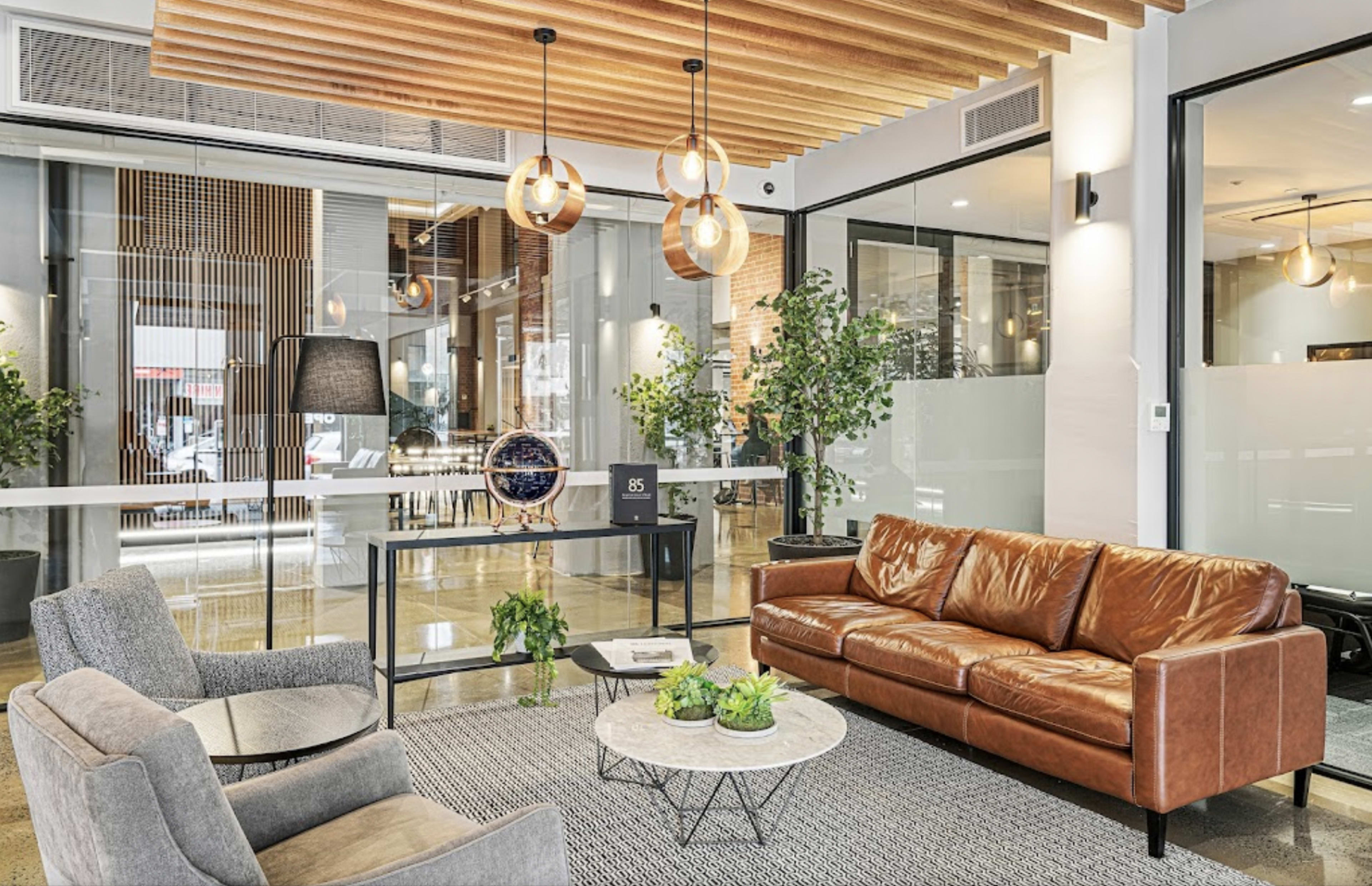 The image shows a modern lounge area with a brown leather sofa, gray armchairs, a round coffee table, and stylish pendant lights above.