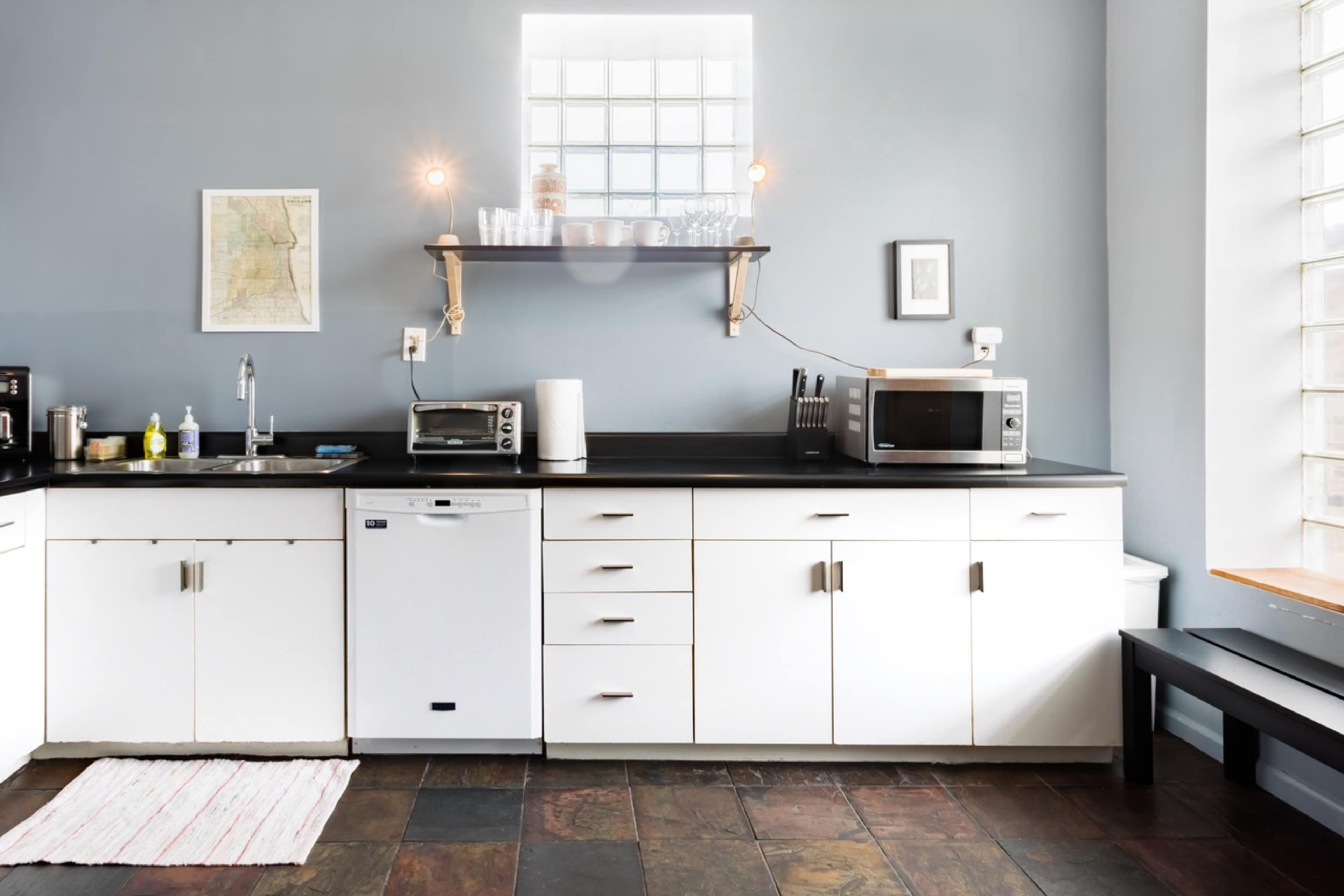 A modern kitchen with white cabinetry, a black countertop, and stainless steel appliances, including a microwave and a dishwasher.
