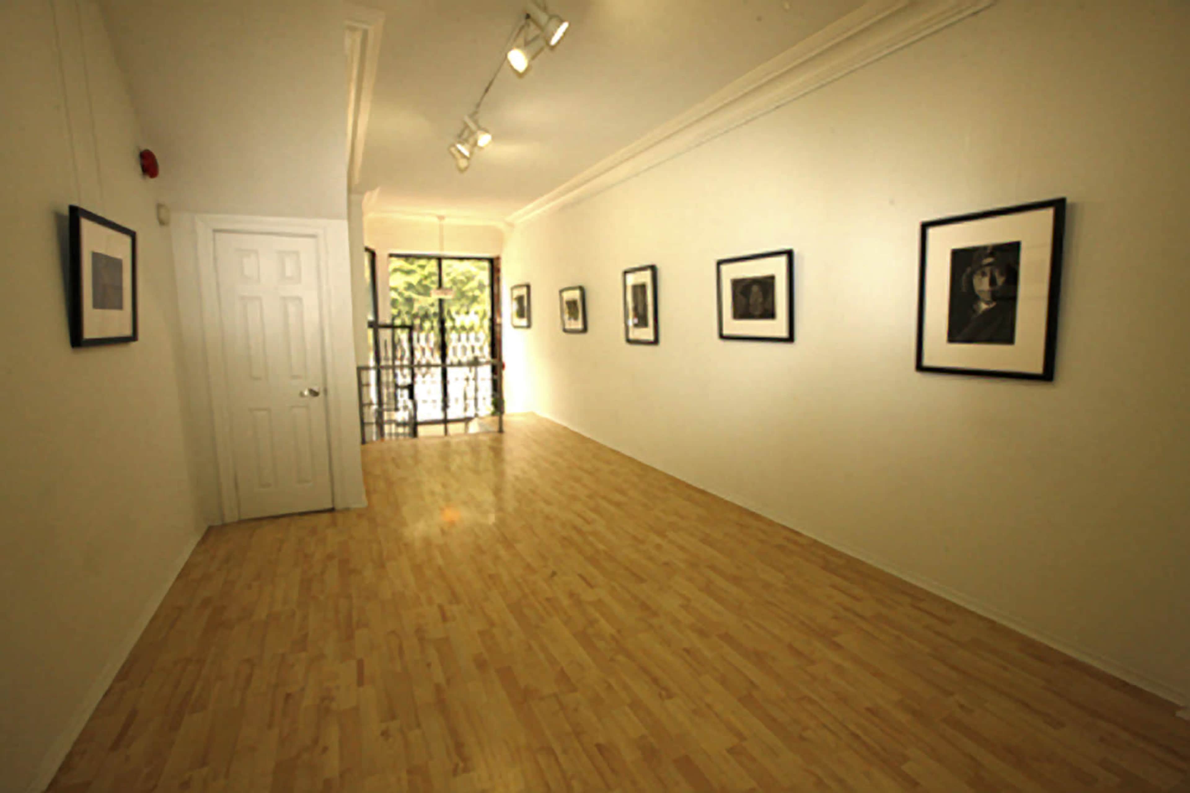 A well-lit art gallery featuring several framed photographs displayed on the white walls, with a door leading to an outdoor area.