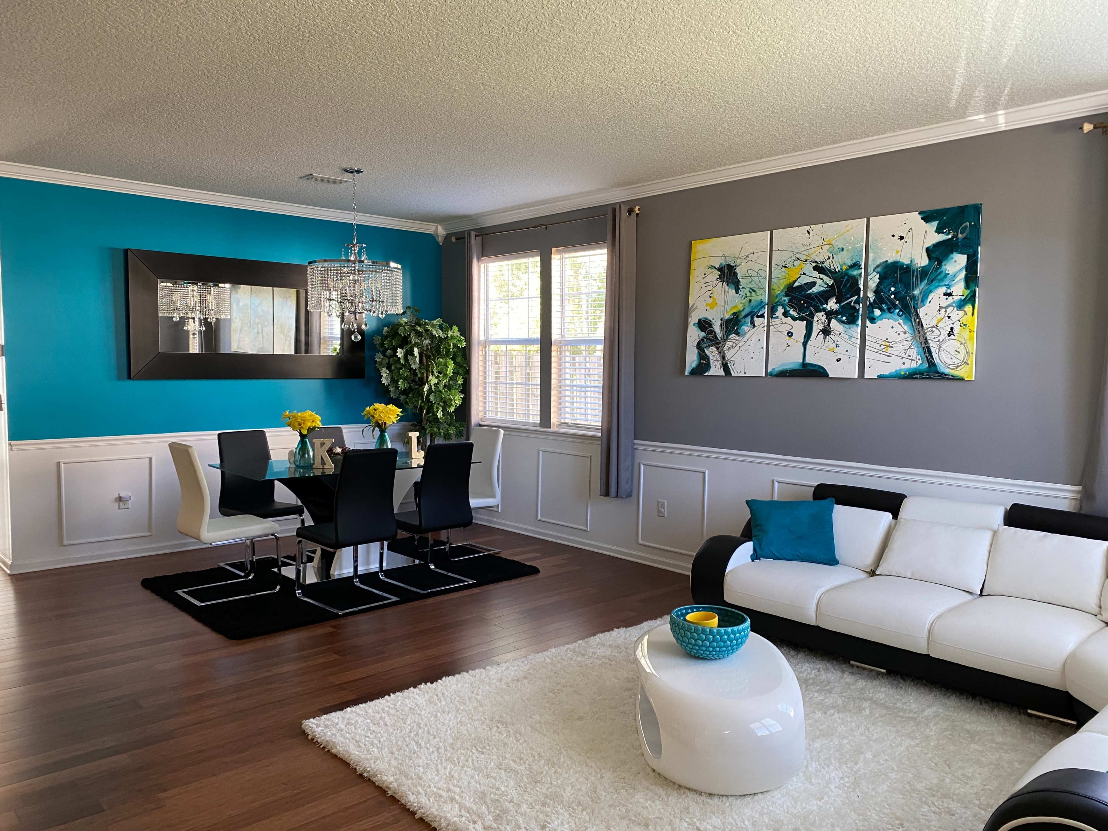A modern living and dining area with a white sofa, a black and white dining table set, and colorful artwork on the wall.