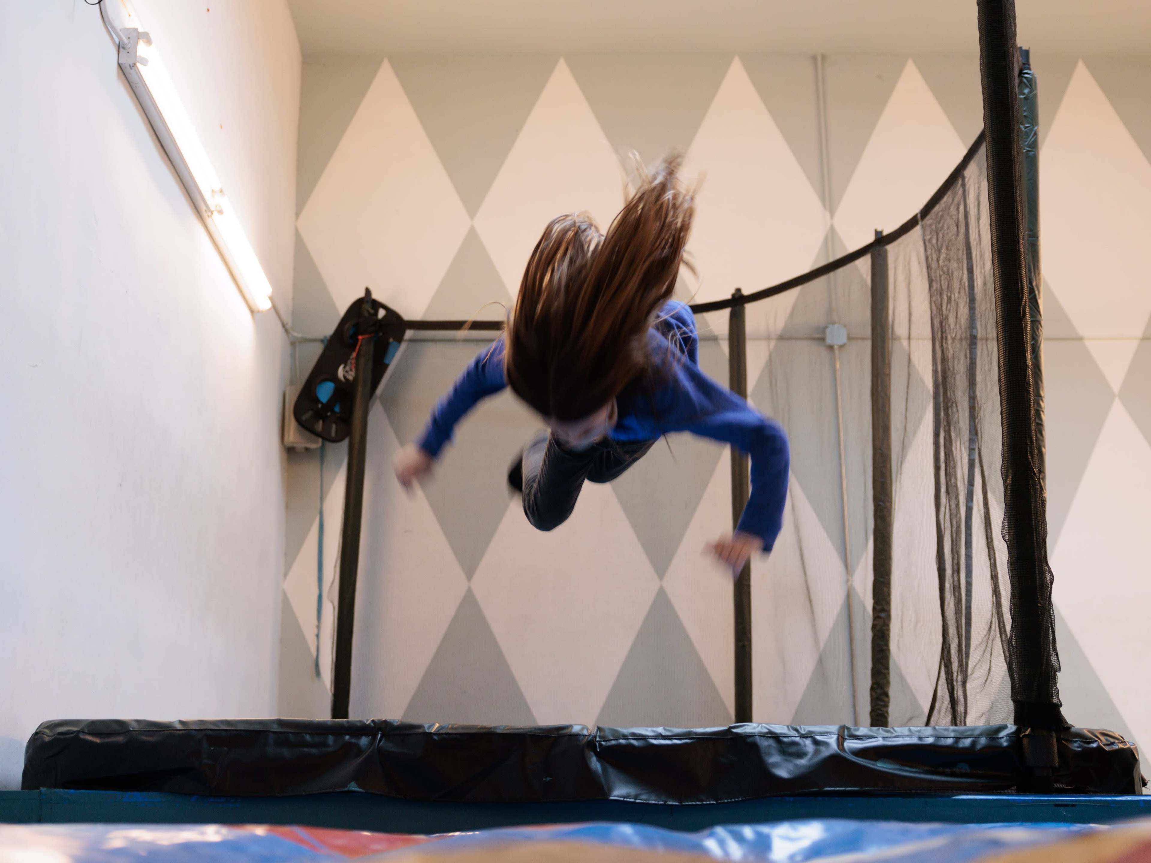 A child jumps off a trampoline in a gym with a geometric patterned wall.