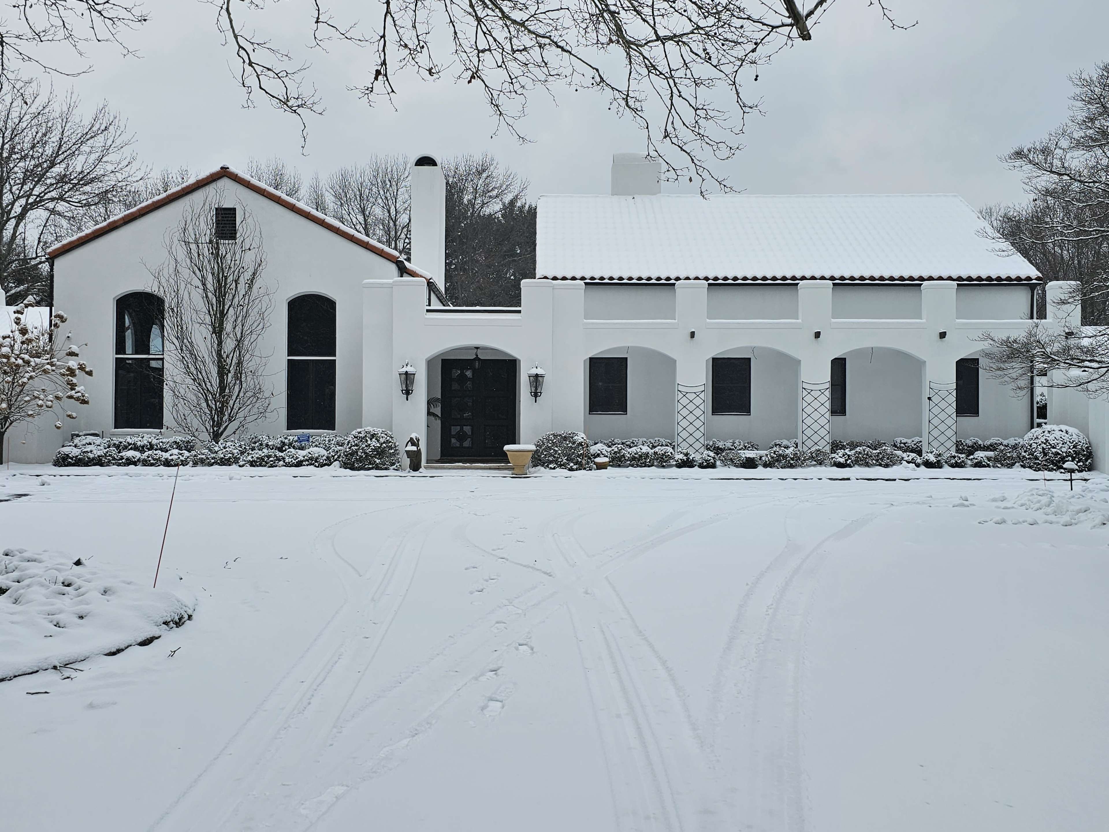A white stucco house with a red-tiled roof is set against a snowy landscape.