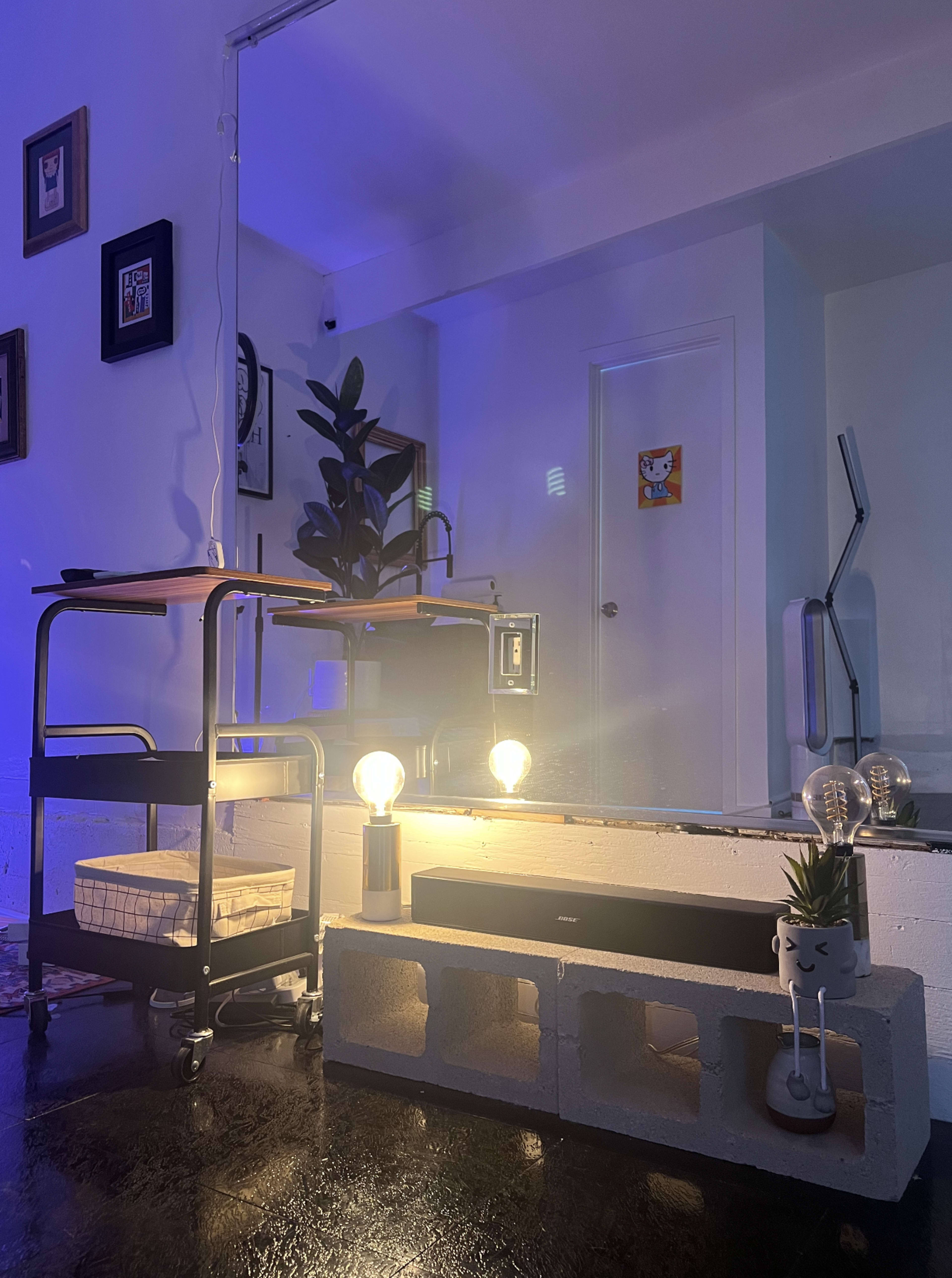 A modern living space features a cart with a plant, a concrete block table with lights, and a wall mirror reflecting the room.