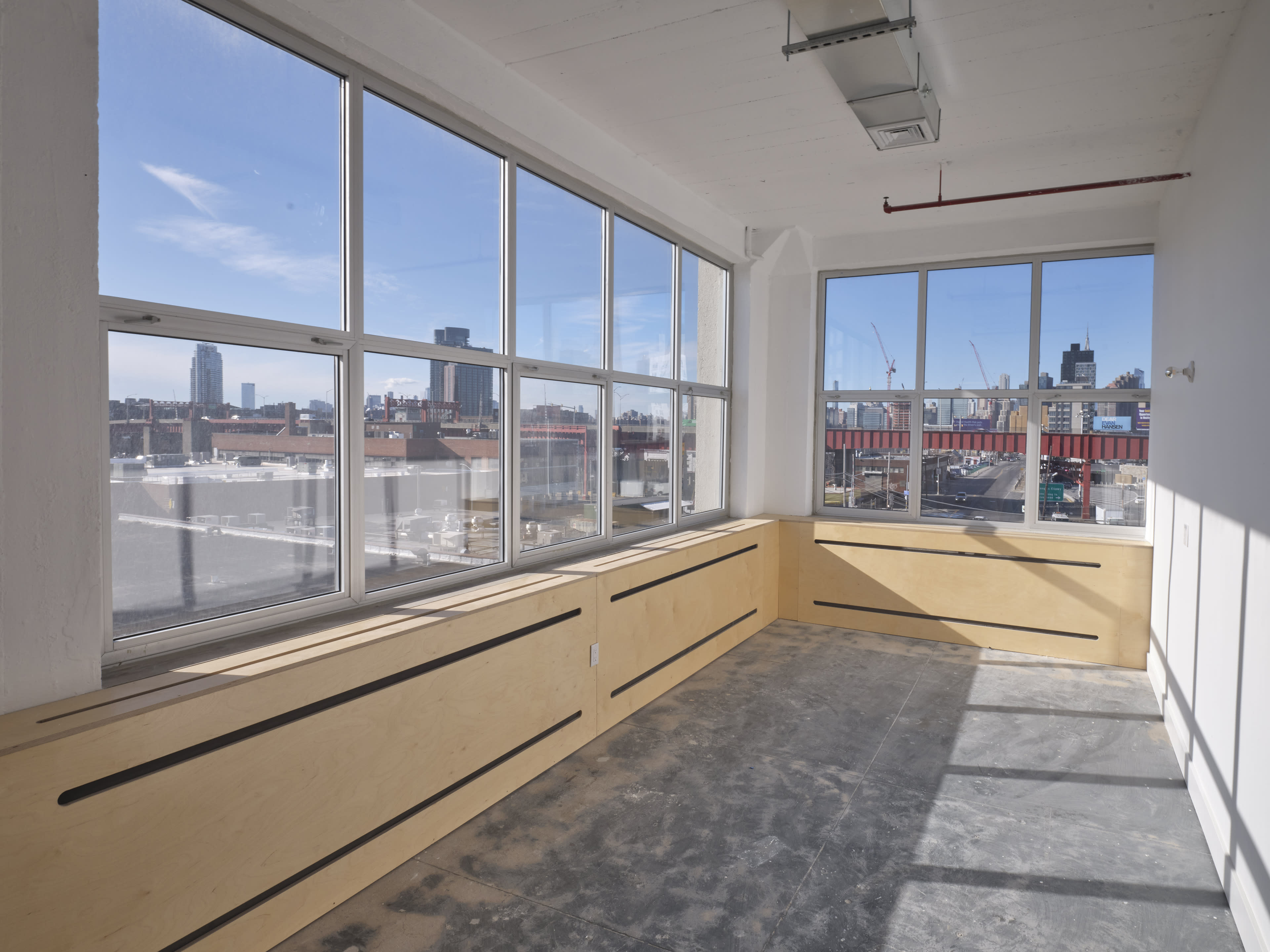 A vacant room with large windows offering an expansive view of a city skyline and construction sites.