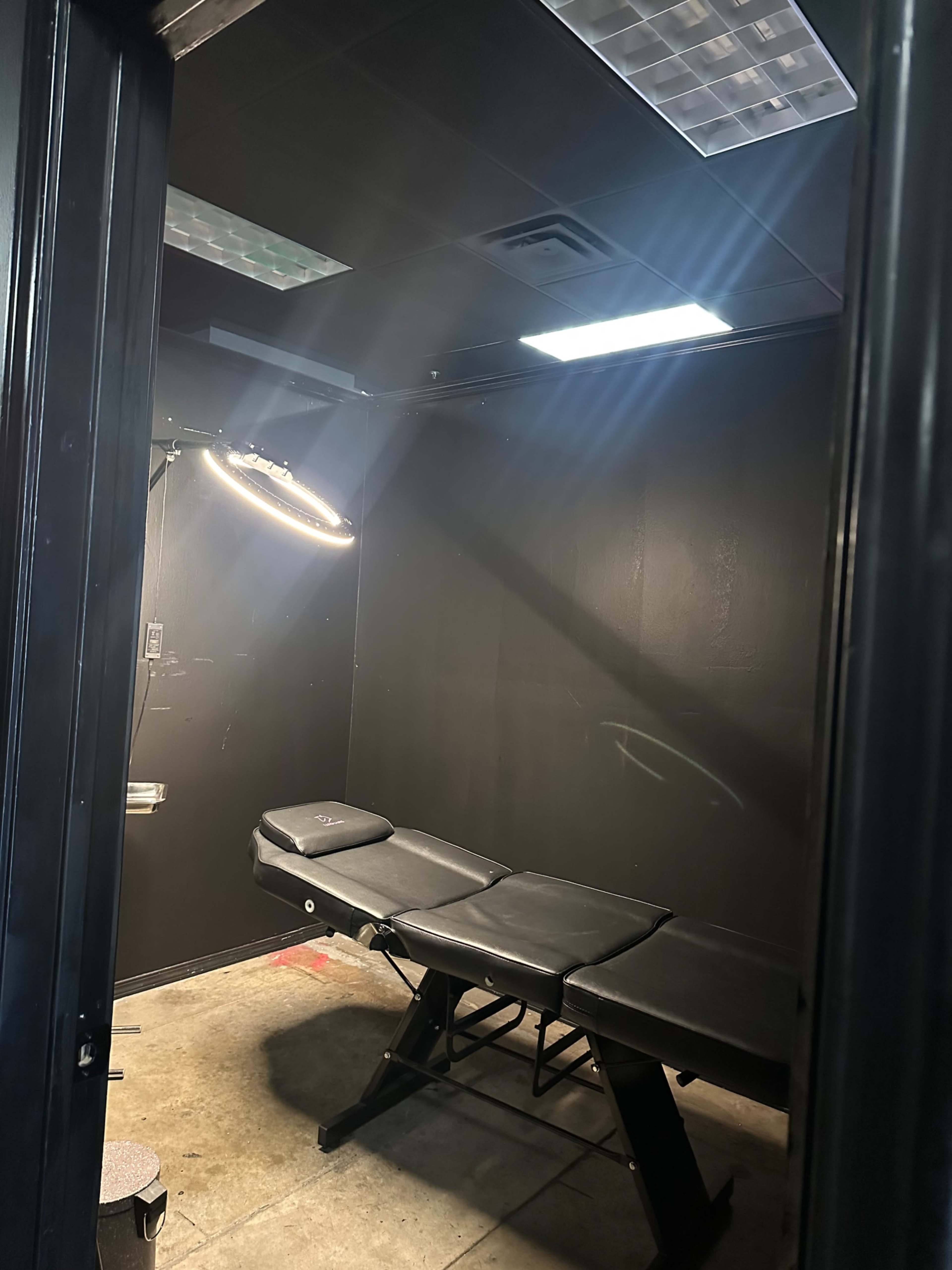 The image shows a small, dimly lit room with a black examination table and a light fixture on the wall.