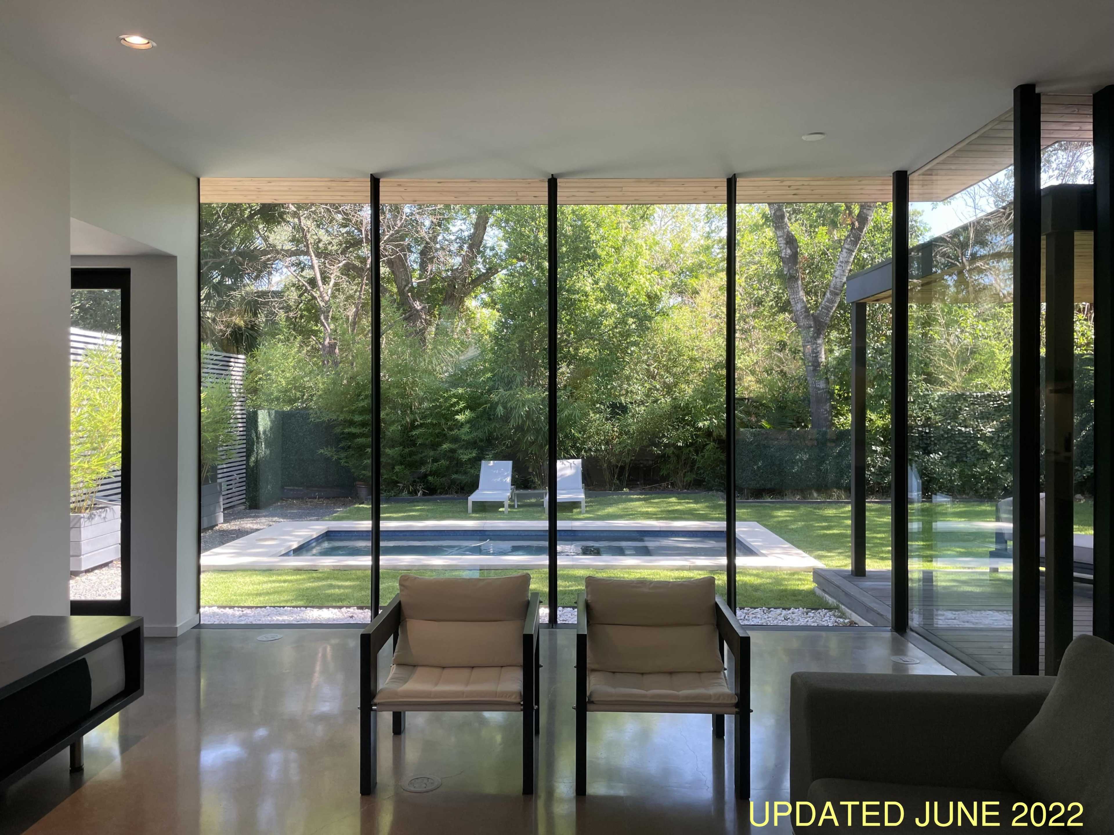A modern interior space with two chairs facing large glass windows that overlook a garden with a pool and two lounge chairs.