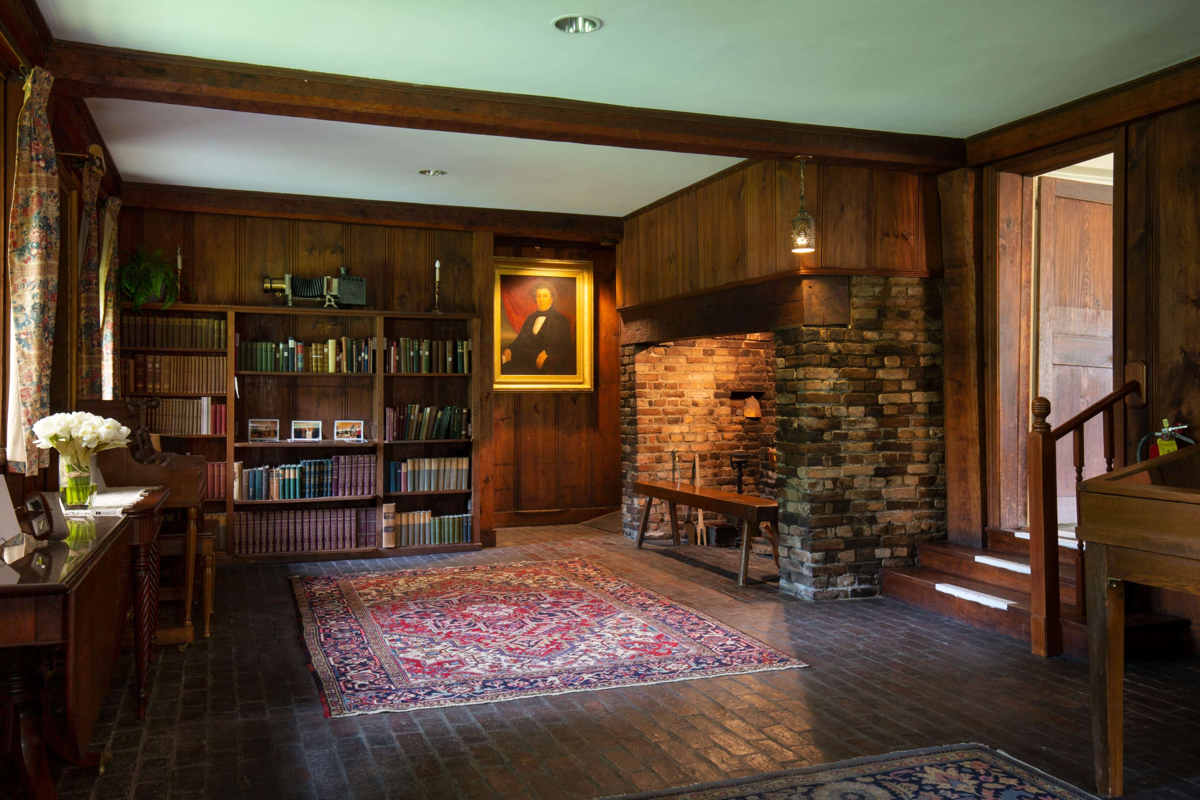 A cozy, wooden room featuring a brick fireplace, shelves filled with books, and a decorative rug on a dark floor.