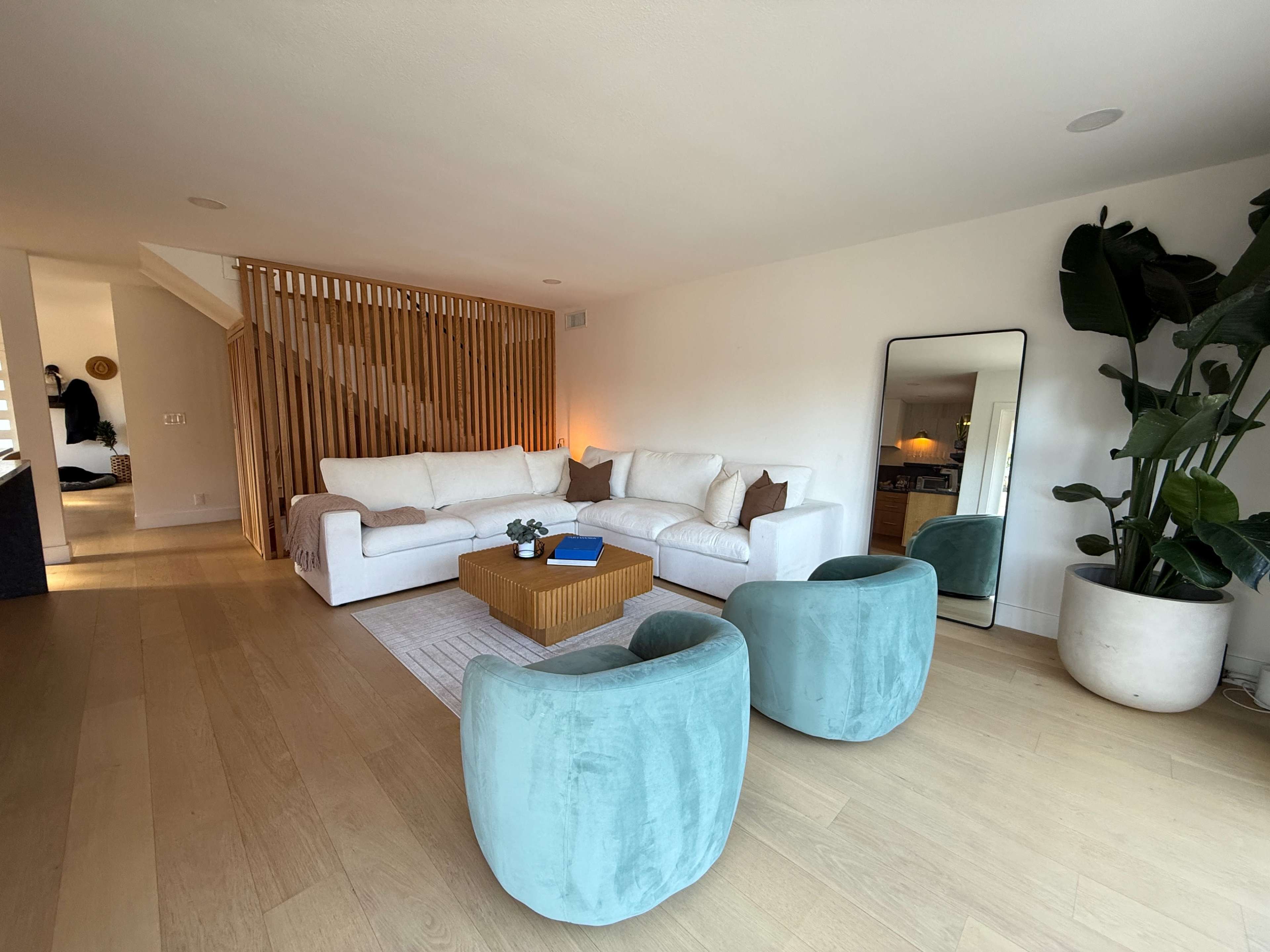 The image showcases a modern living room featuring a white sectional sofa, a wooden accent table, two light blue chairs, and a large potted plant.