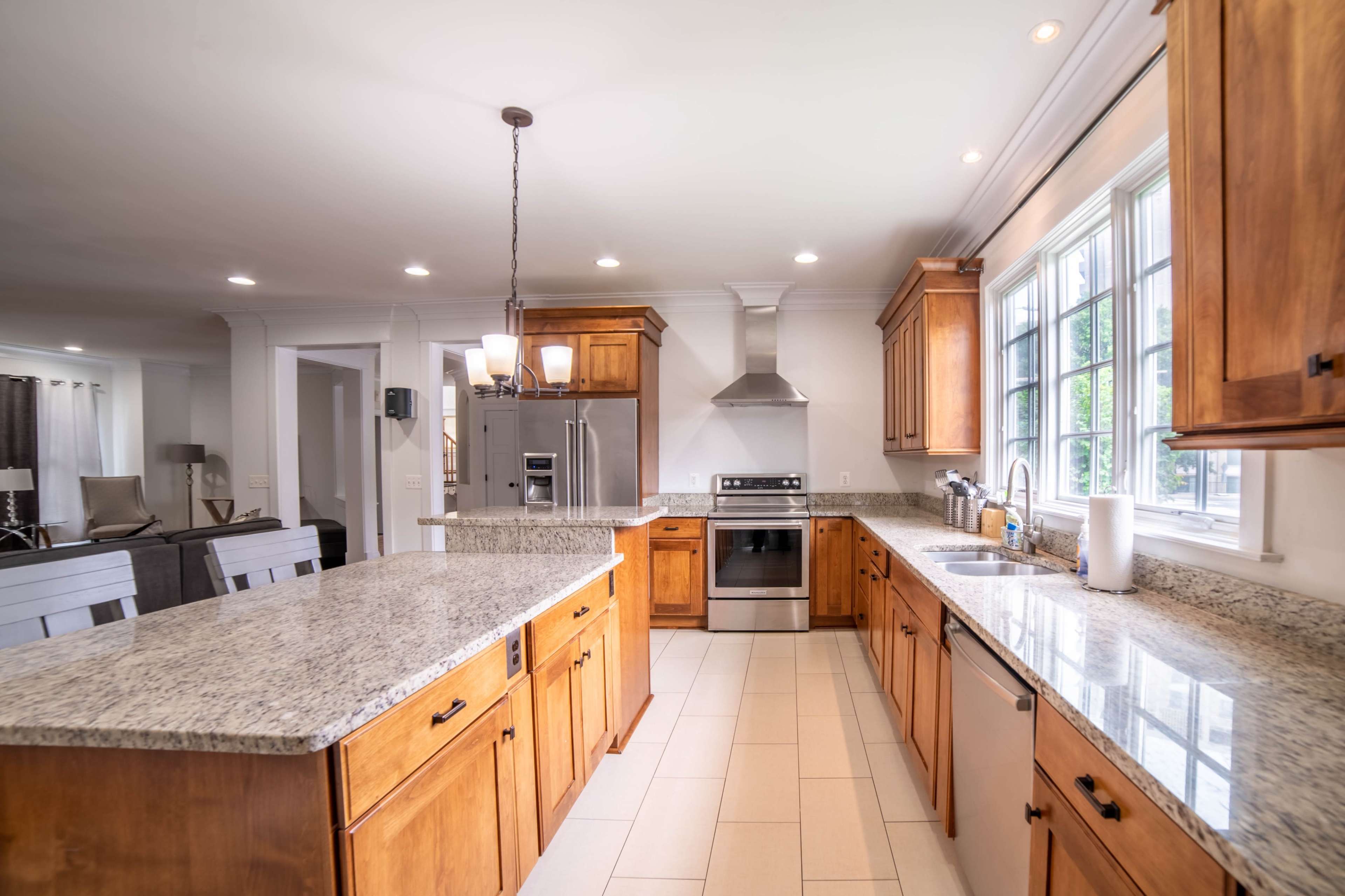 A modern kitchen features wooden cabinets, granite countertops, stainless steel appliances, and a central island with seating.