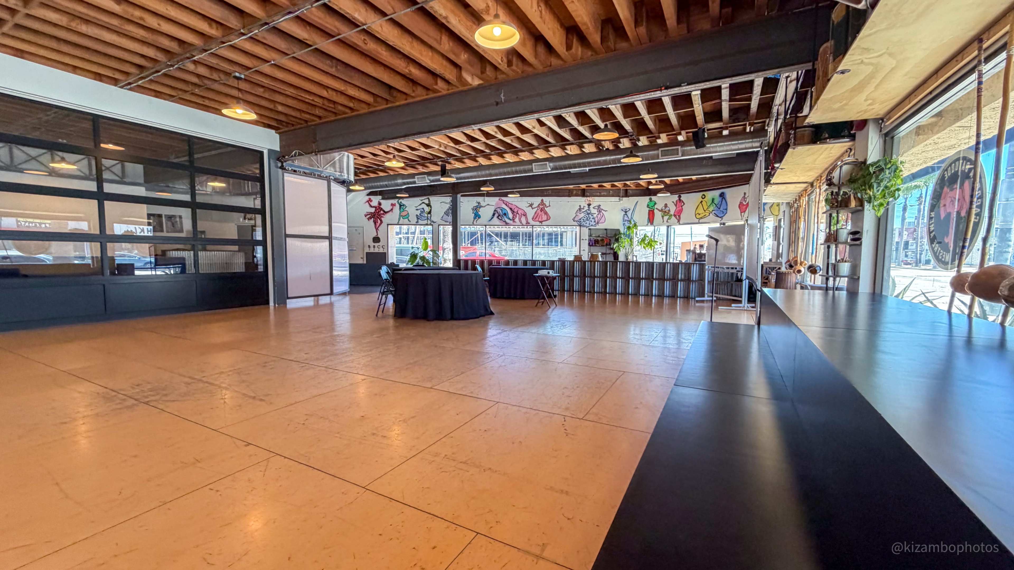 The image shows a spacious, open interior with a polished floor, large windows, and colorful artwork displayed on the walls.