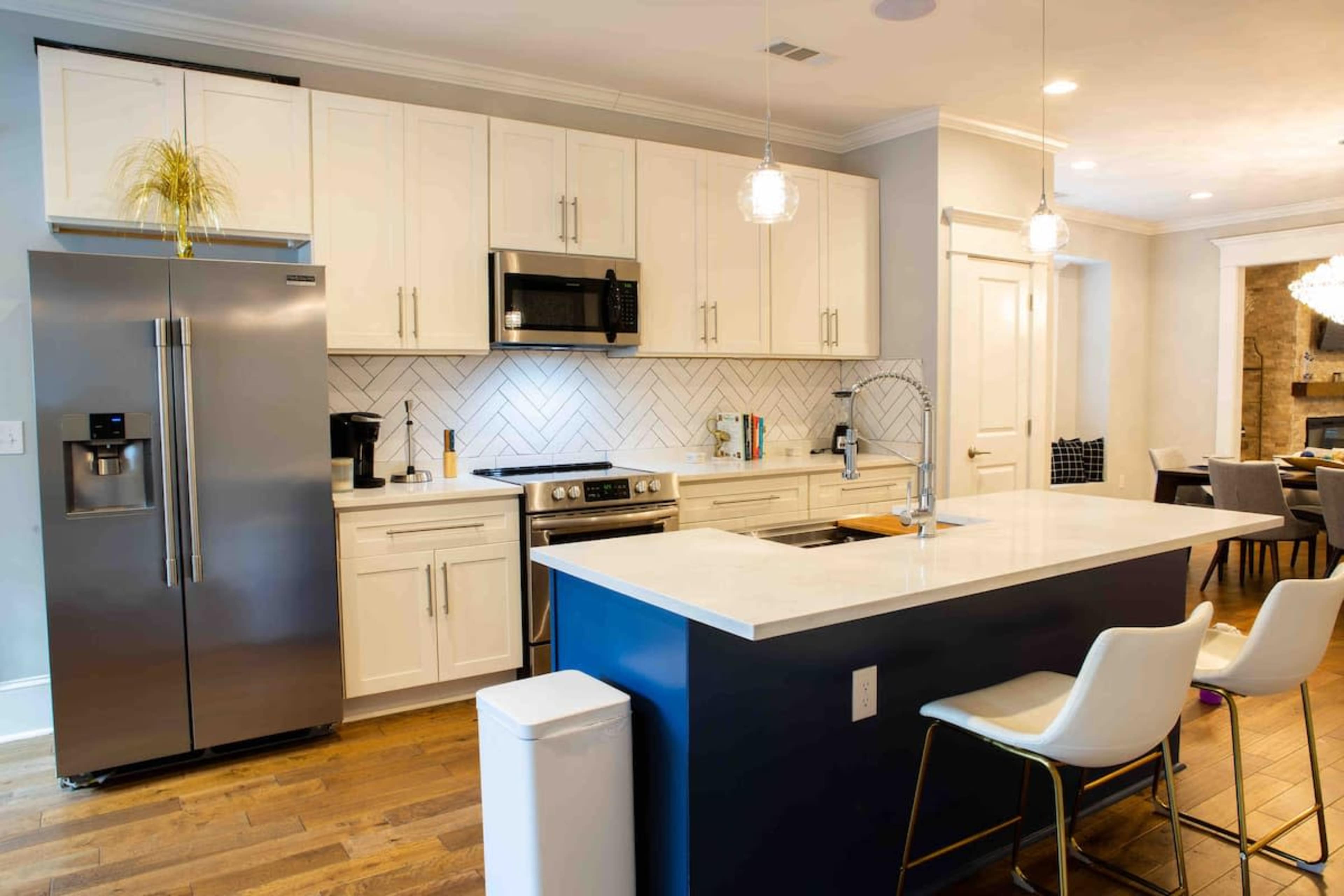 A modern kitchen featuring white cabinets, stainless steel appliances, a large island with seating, and a herringbone tile backsplash.