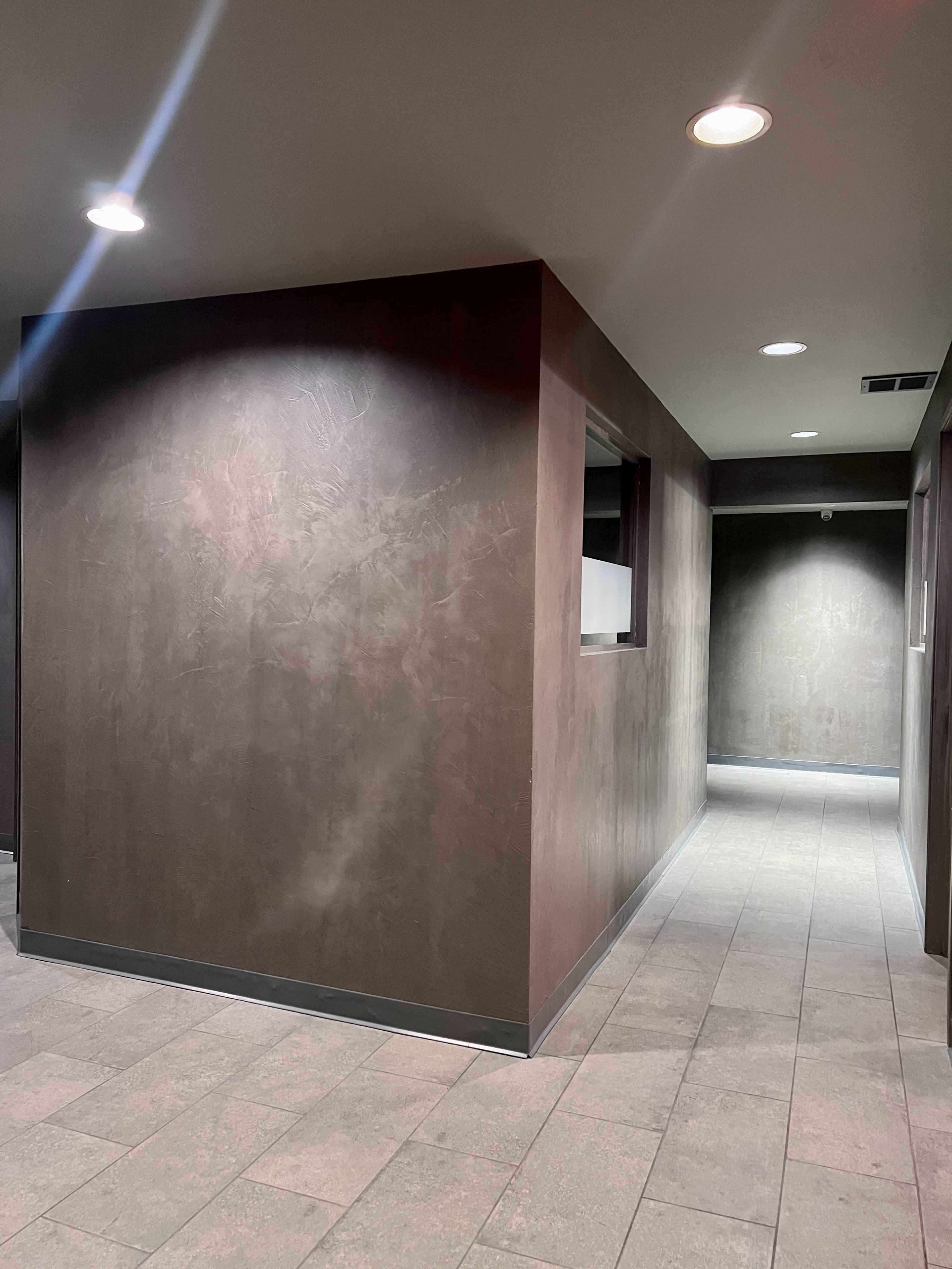 A dimly lit corridor with textured walls and tiled flooring, leading to an open space on the left.