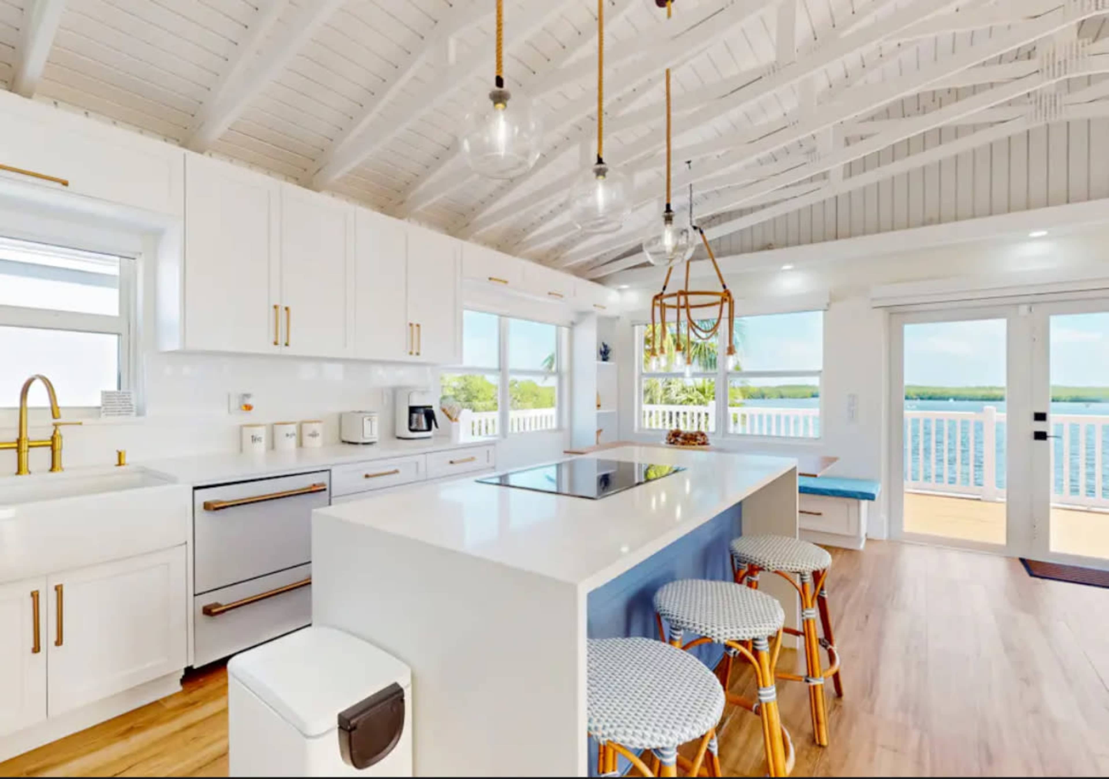 A modern kitchen features white cabinetry, a central island with a cooktop, and large windows overlooking a scenic view.