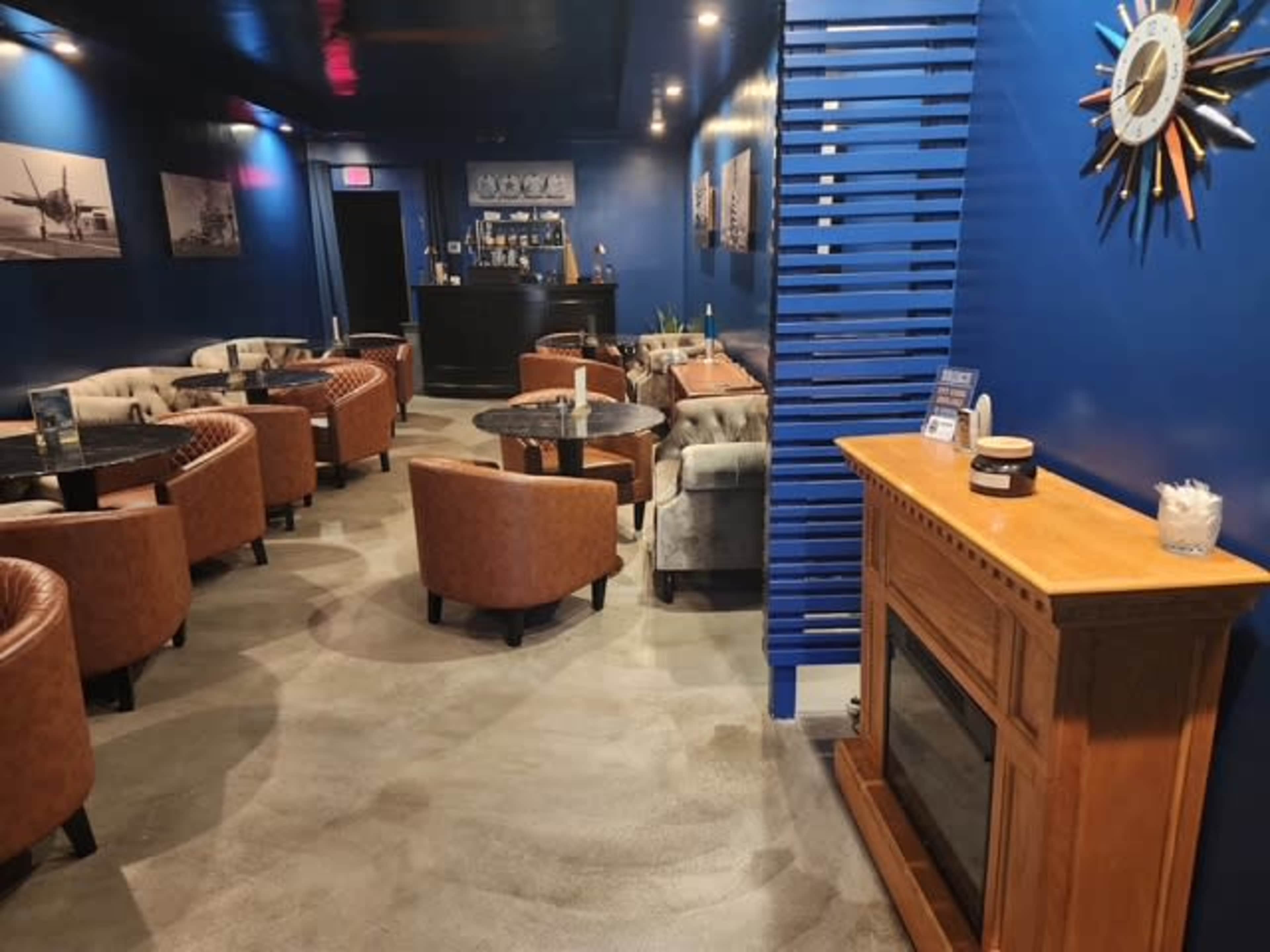 The image shows a dimly lit lounge with leather seating, wooden furniture, and a bar in the background, surrounded by blue walls and framed photographs.