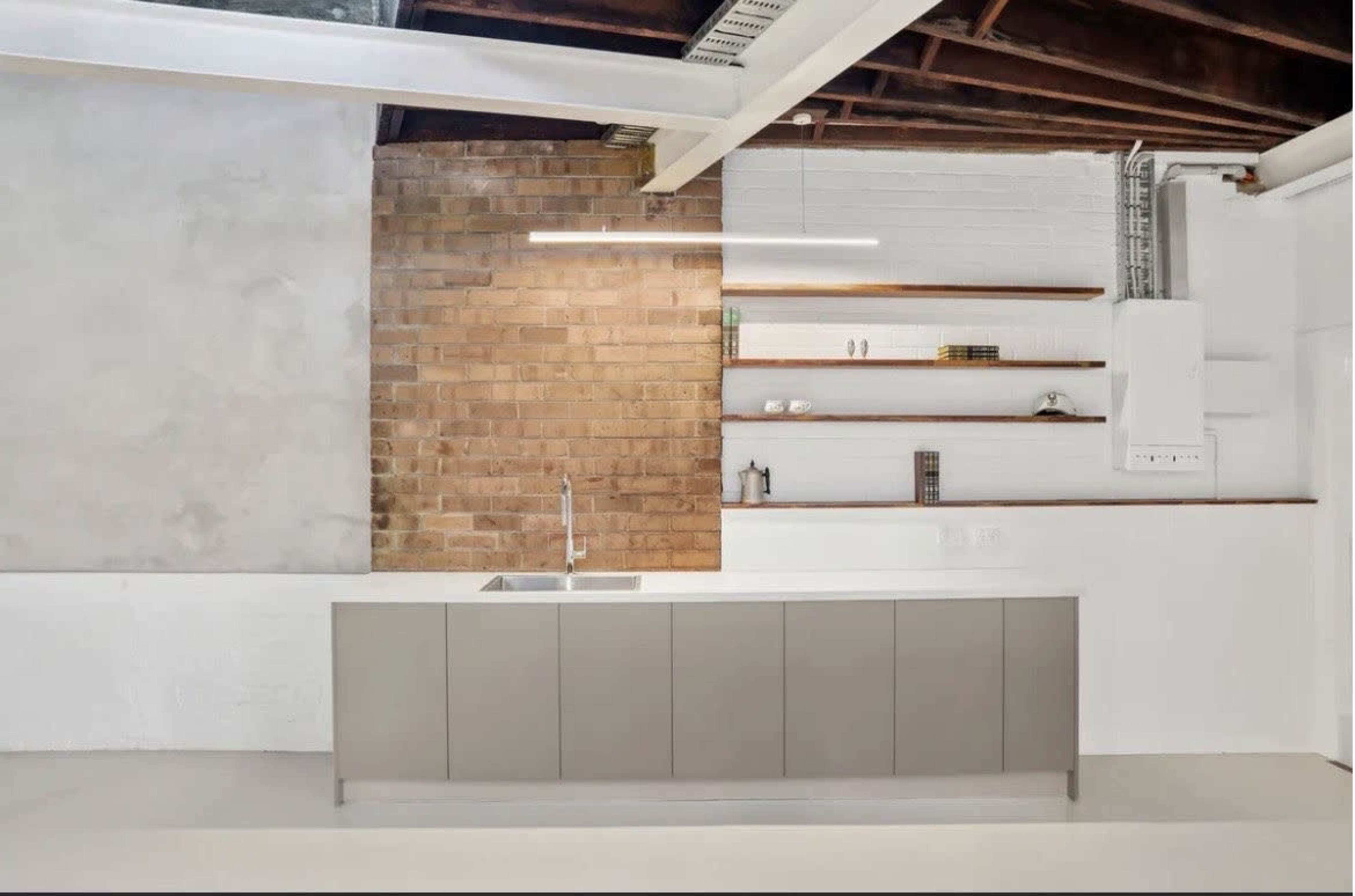 The image shows a modern kitchen with a central island, a brick accent wall, and open shelves above.