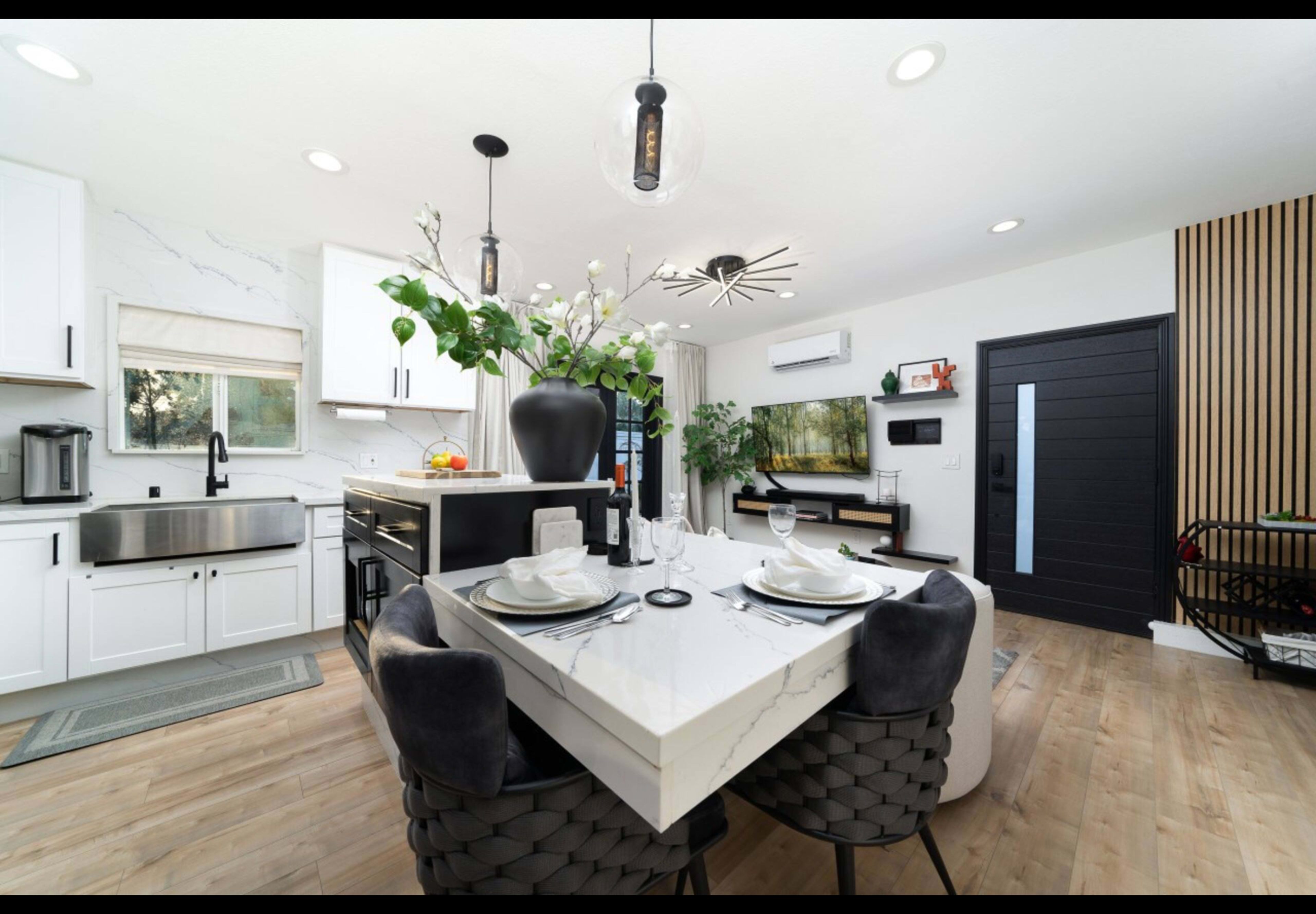 A modern kitchen and dining area features a marble table set for four, sleek cabinetry, and large windows allowing natural light.