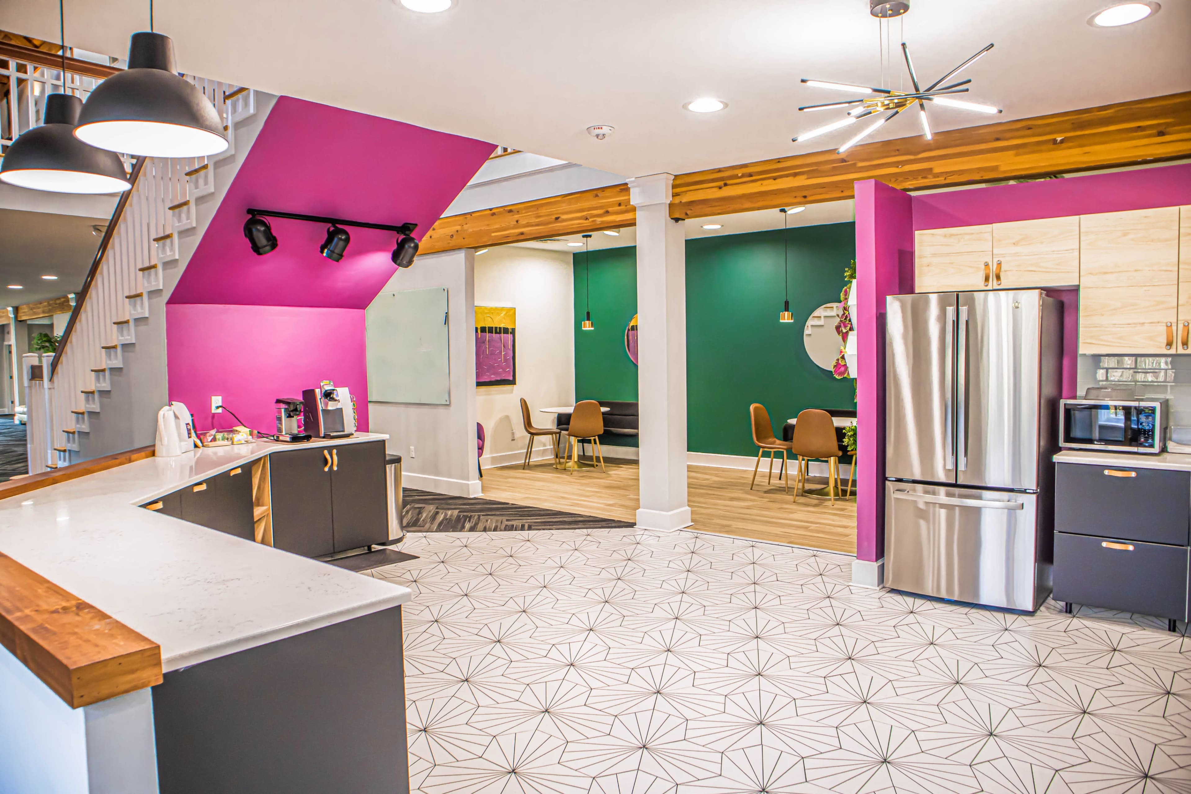 A modern open-concept space with a kitchen area featuring a stainless steel refrigerator and a seating area with chairs, walls painted in vibrant colors, and a staircase in the background.