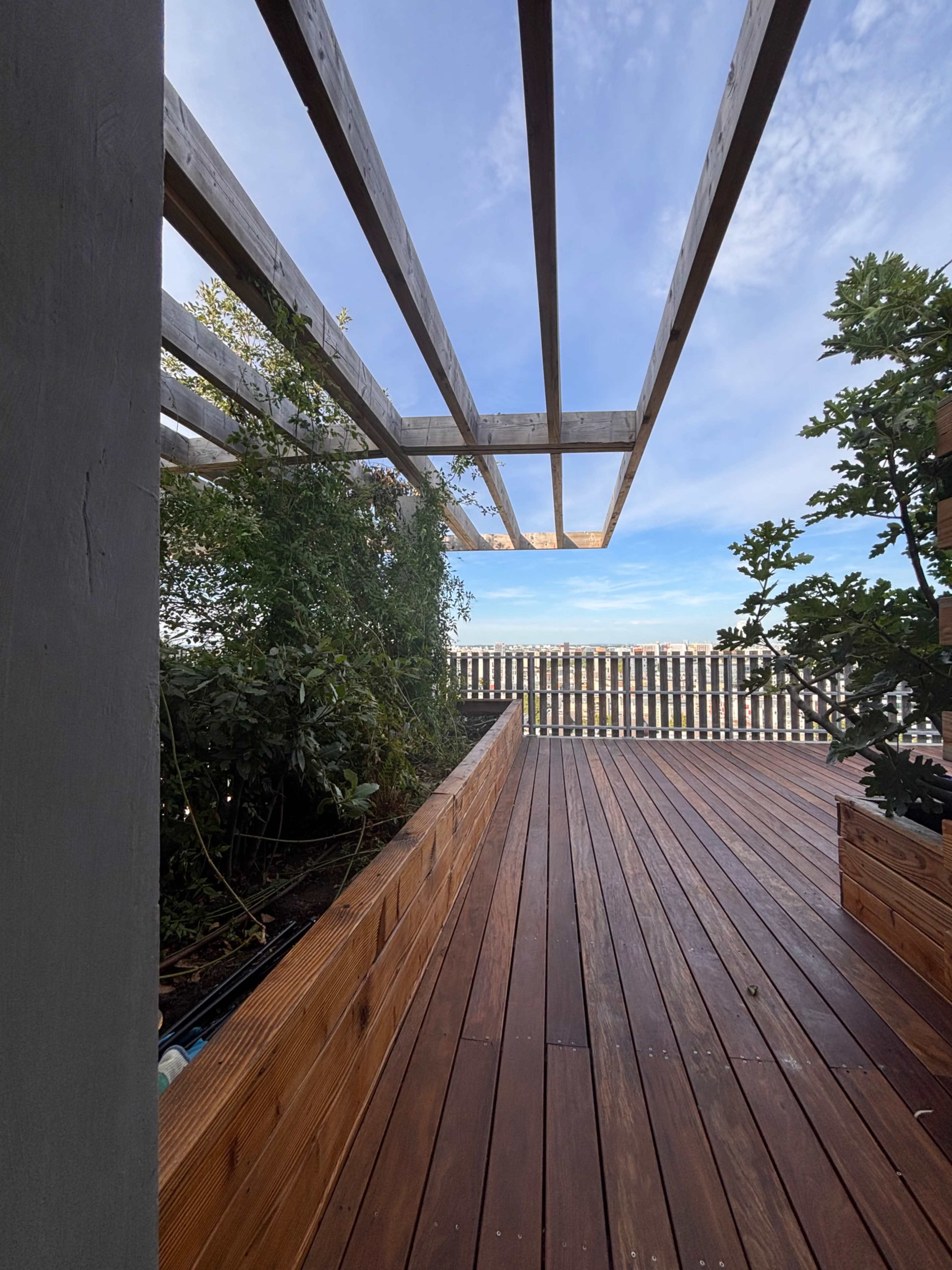 A wooden deck with a slatted pergola and greenery is visible under a blue sky.