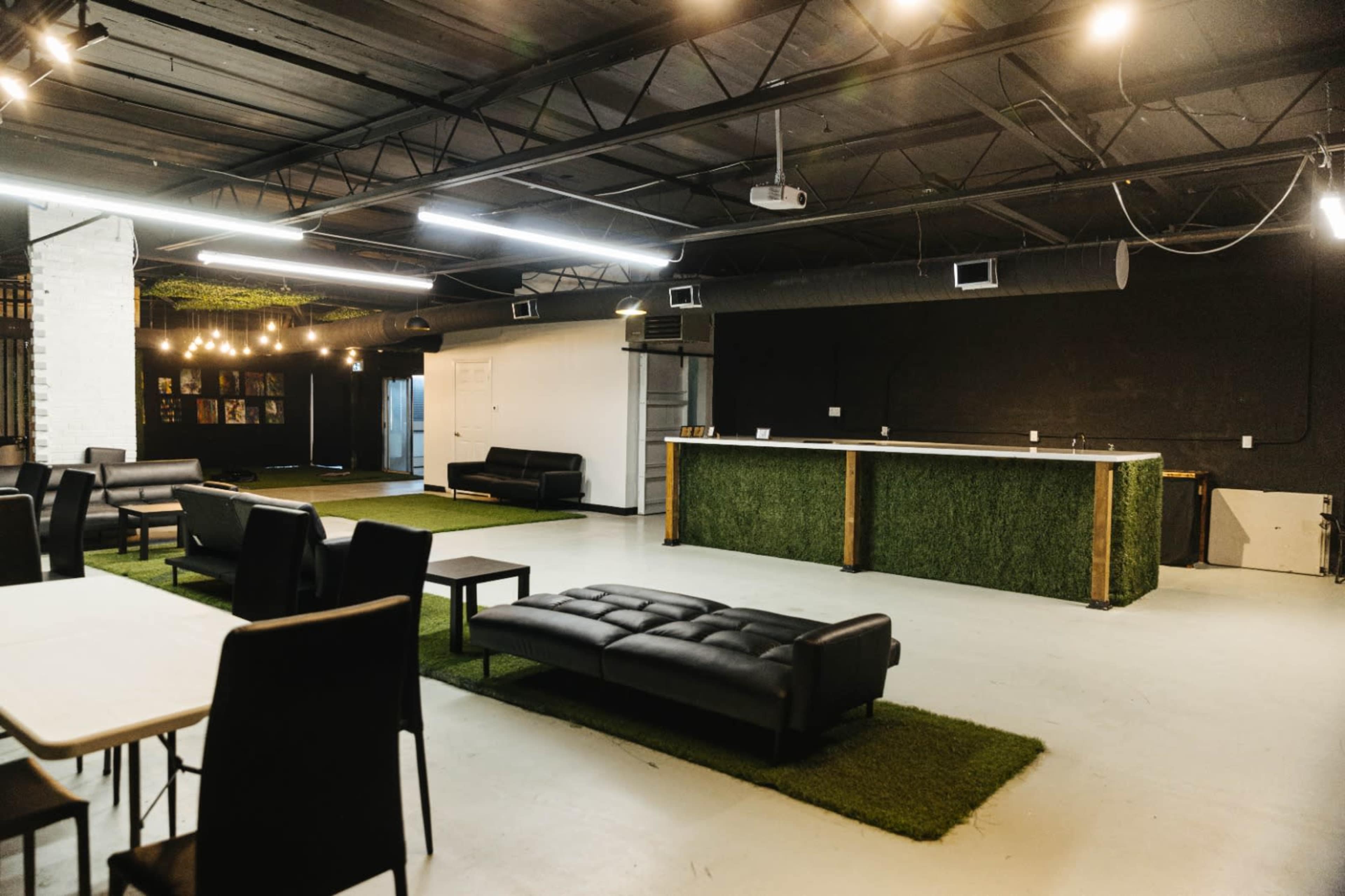 A spacious, modern lounge area with black sofas, a bar counter, and green turf sections on the floor.