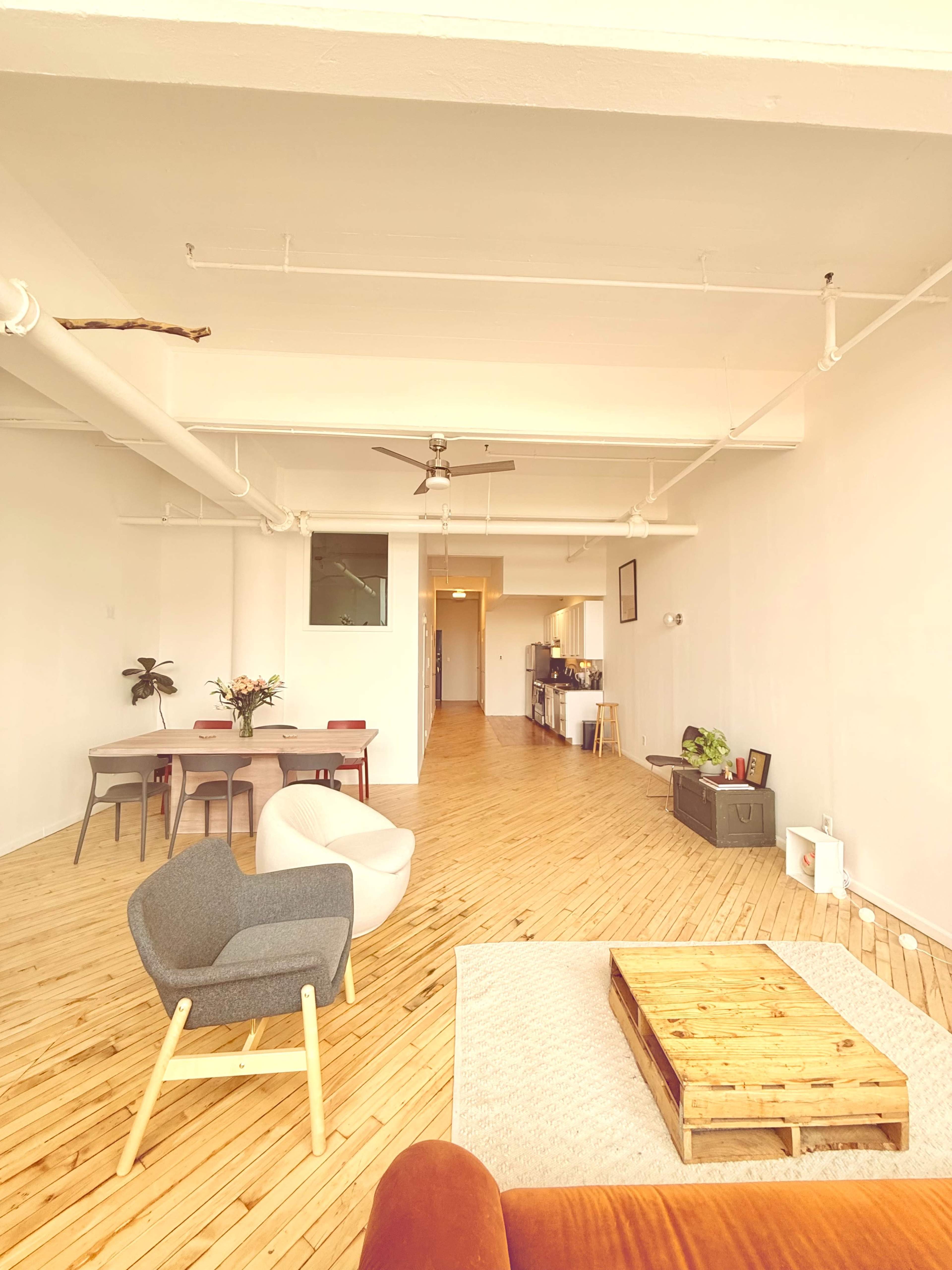 The image shows a spacious, open-concept living area with wooden flooring, a dining table, and a modern kitchen in the background.