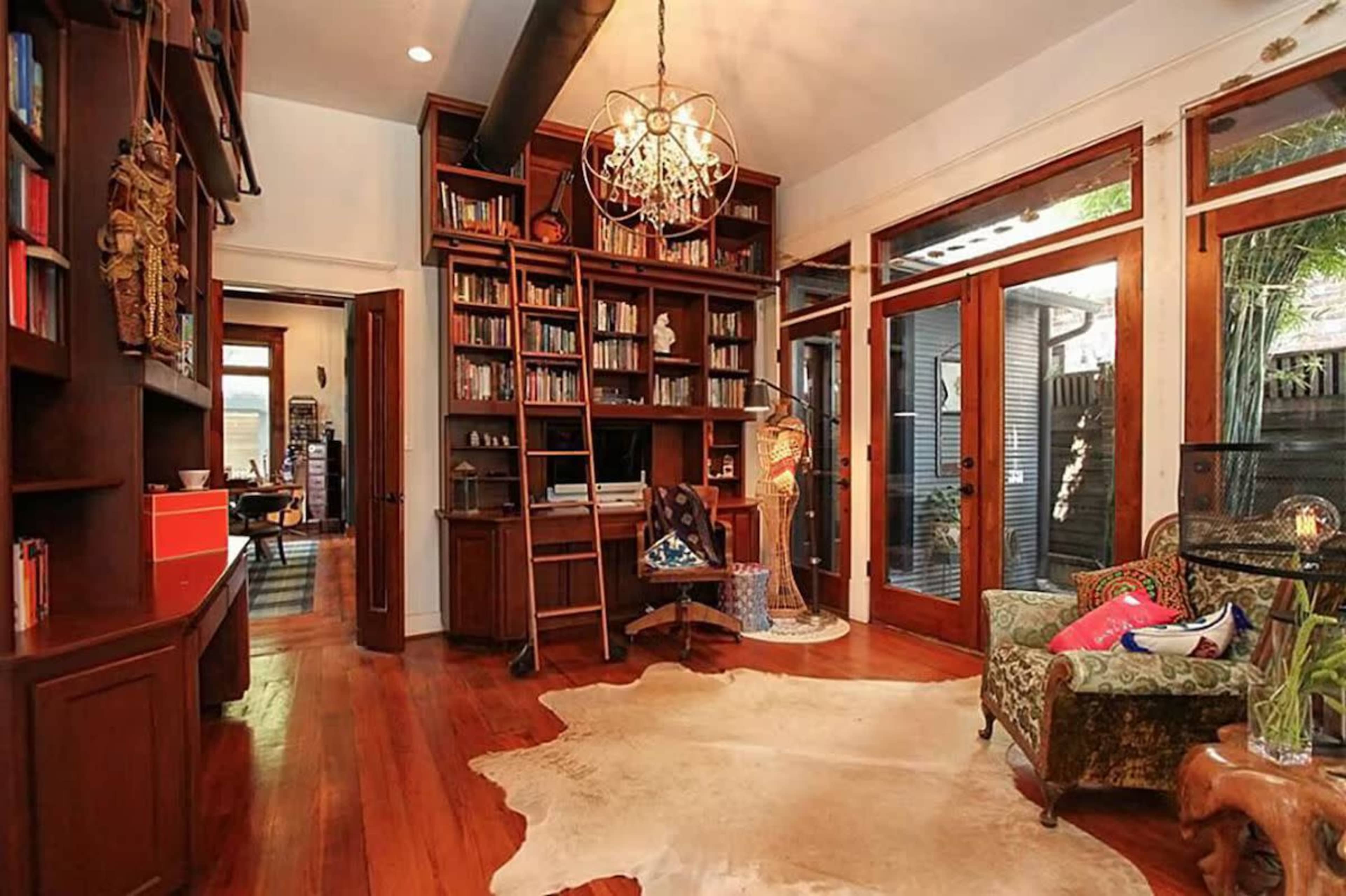 A spacious room with wooden floors, built-in bookshelves filled with books, and large glass doors that open to an outdoor area.