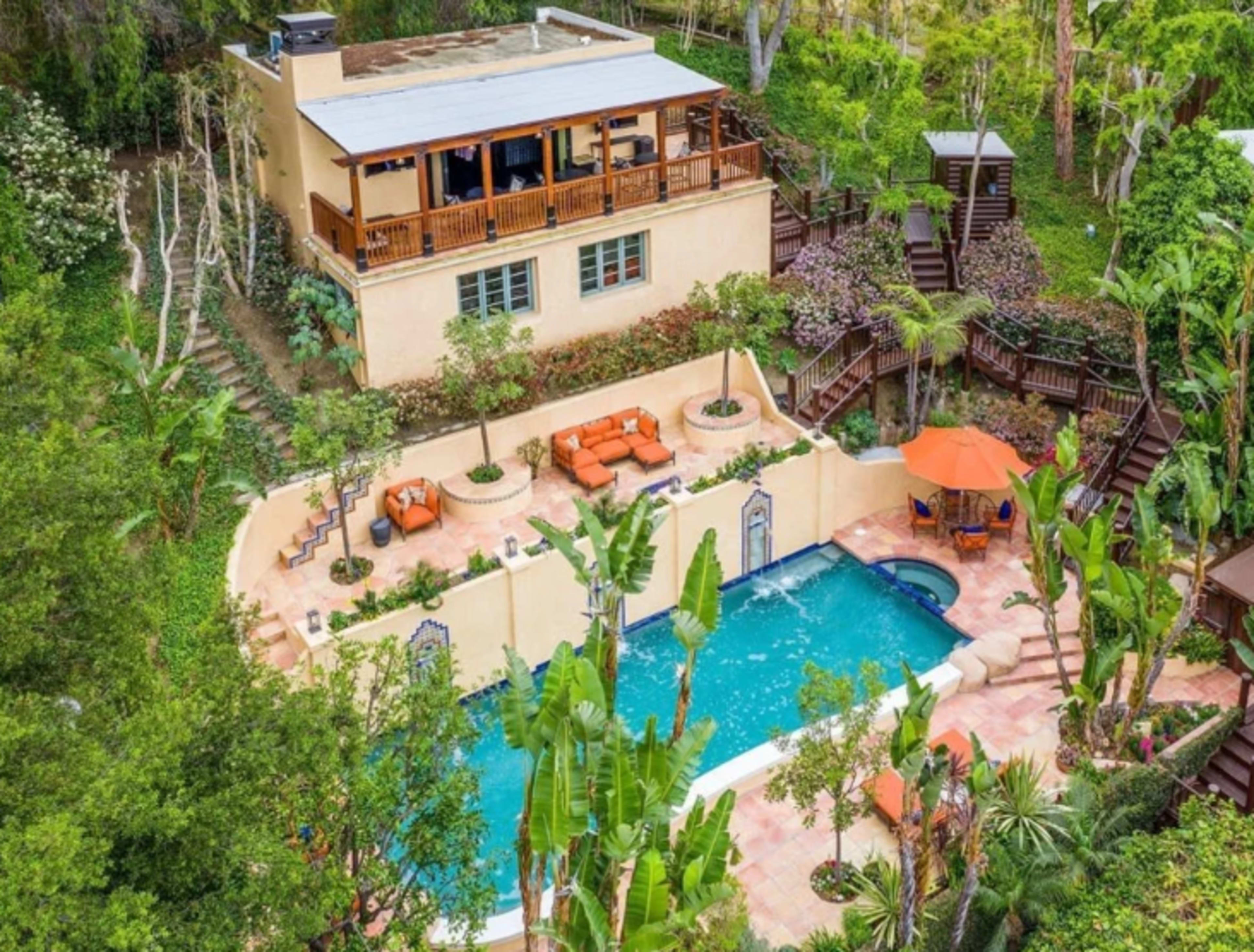 A spacious house overlooking a pool surrounded by tropical plants and lounge areas.