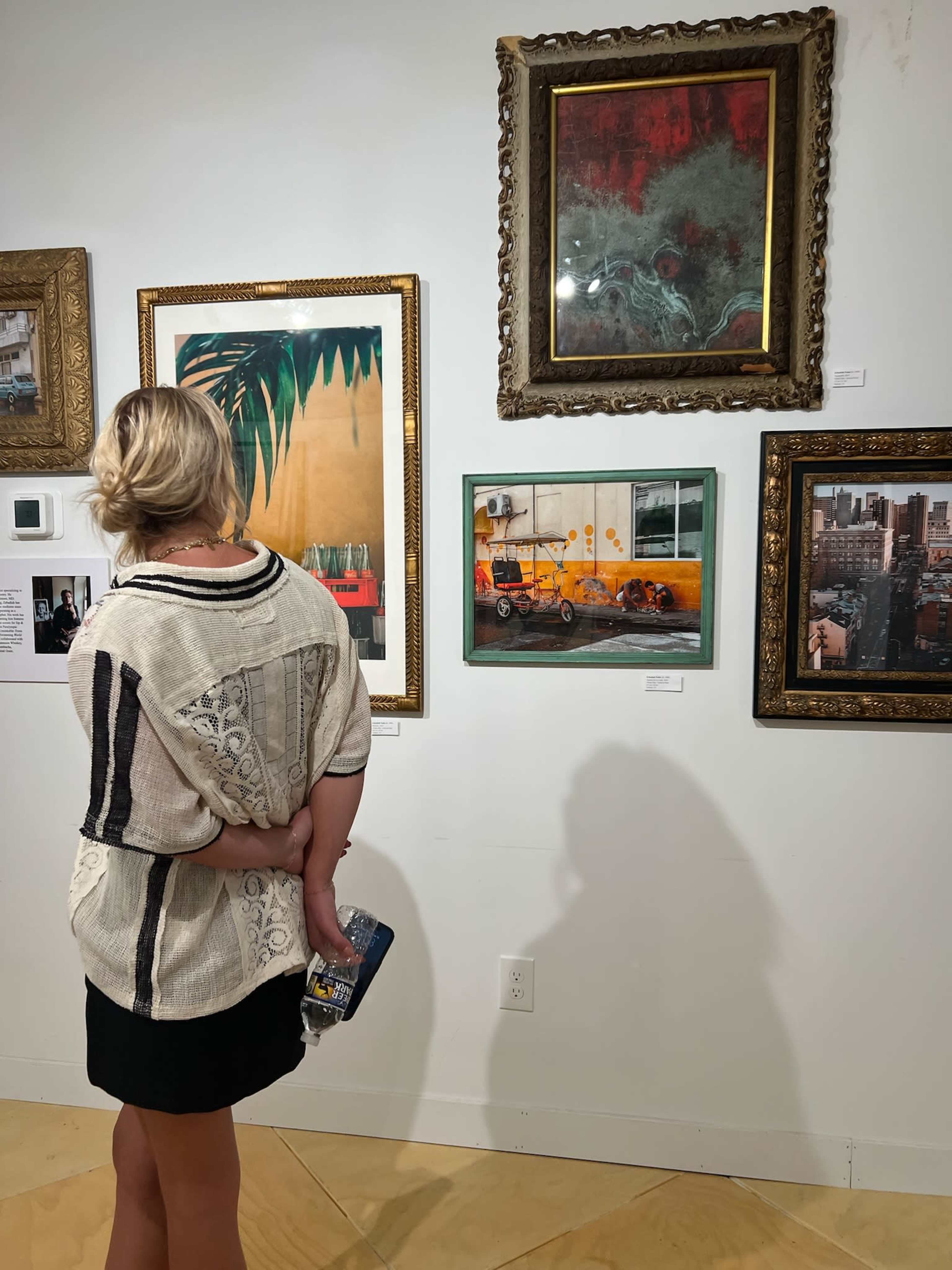 A woman stands in an art gallery, observing a collection of framed artworks on the wall.
