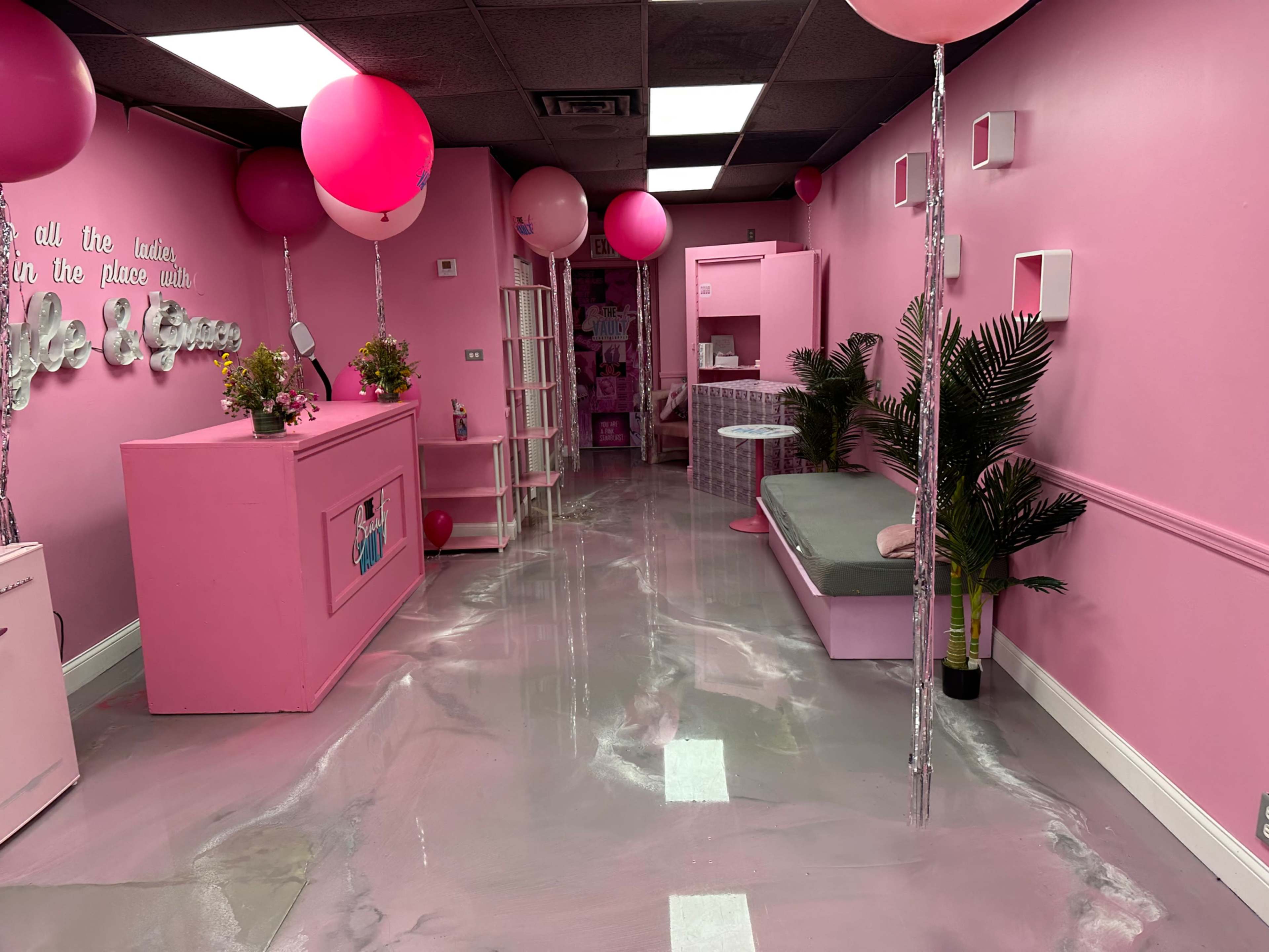 A vibrant pink-themed interior of a store or salon, featuring a reception area, seating, and decorations with balloons and plants.