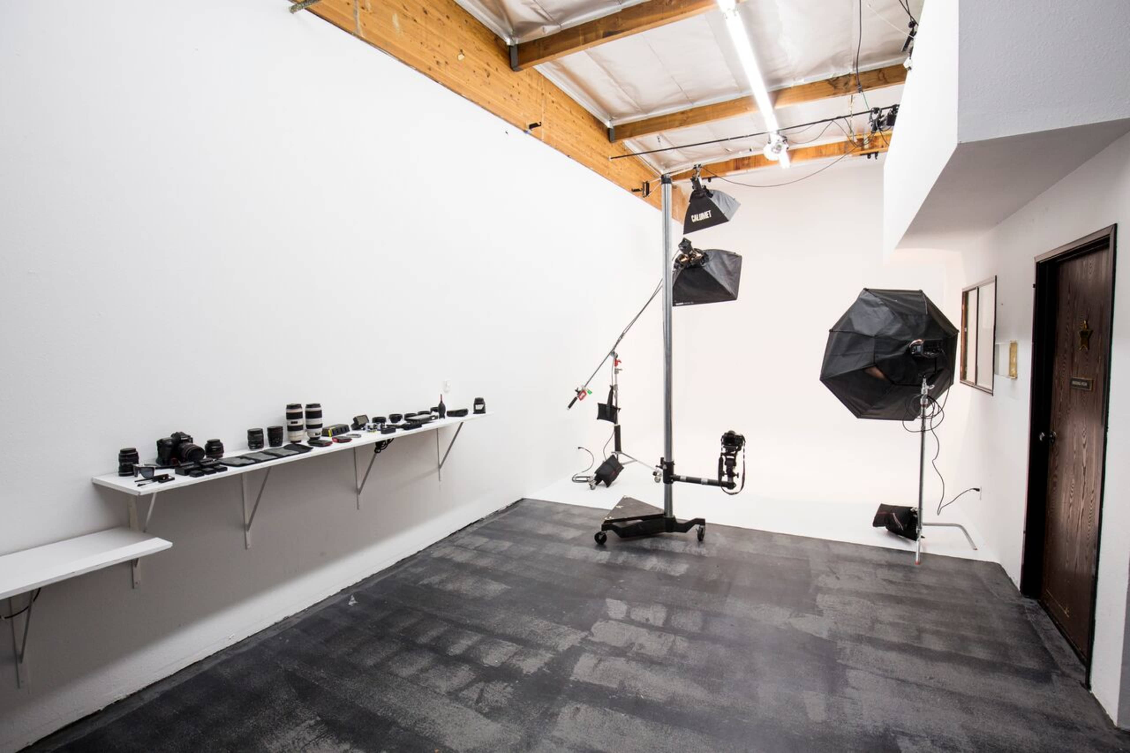 A photography studio with a variety of camera lenses on a shelf, a light stand with softboxes, and a clear, uncluttered space on the floor.