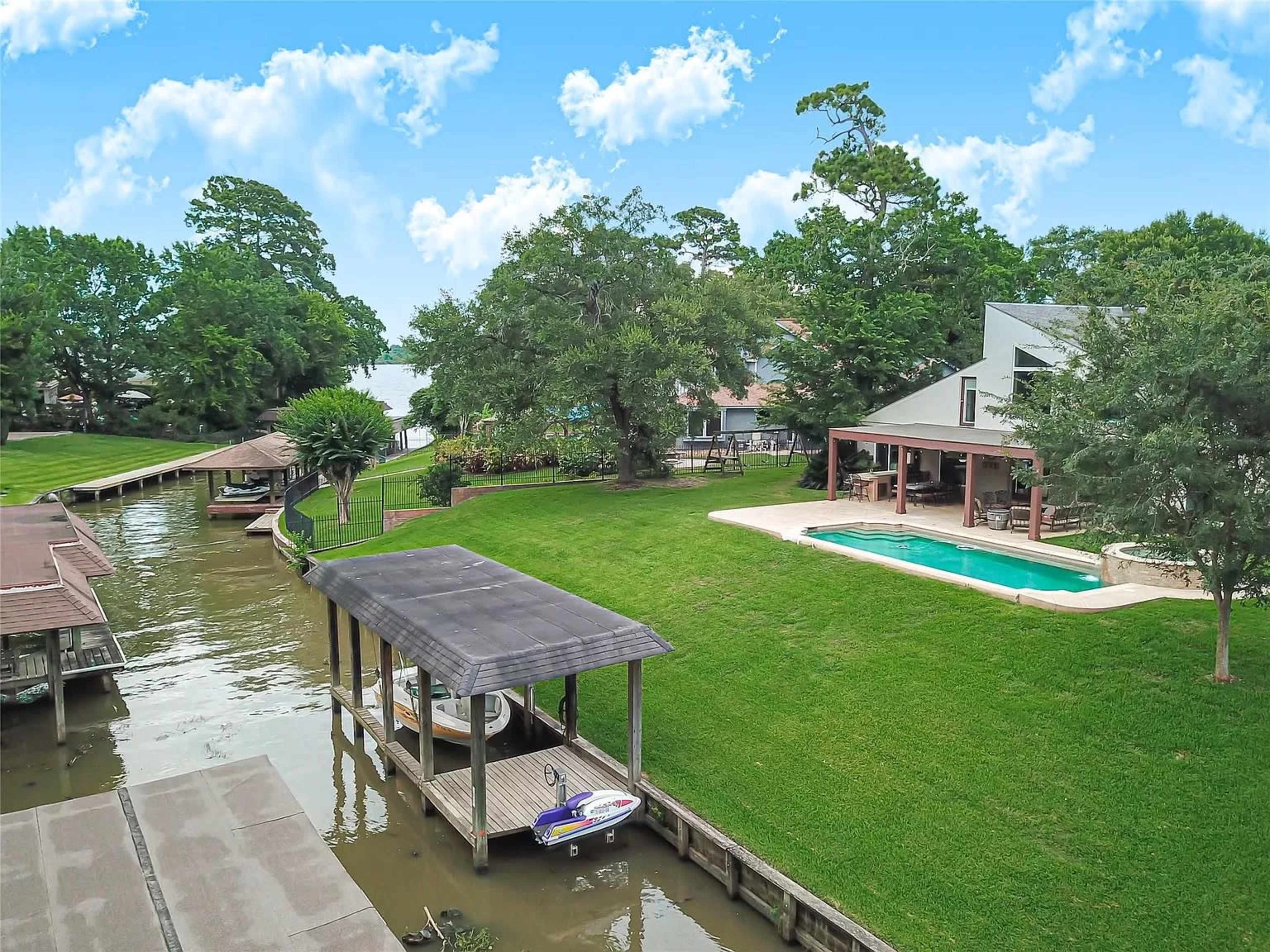 A waterfront property with a pool, dock, and a view of a lake, surrounded by lush greenery.