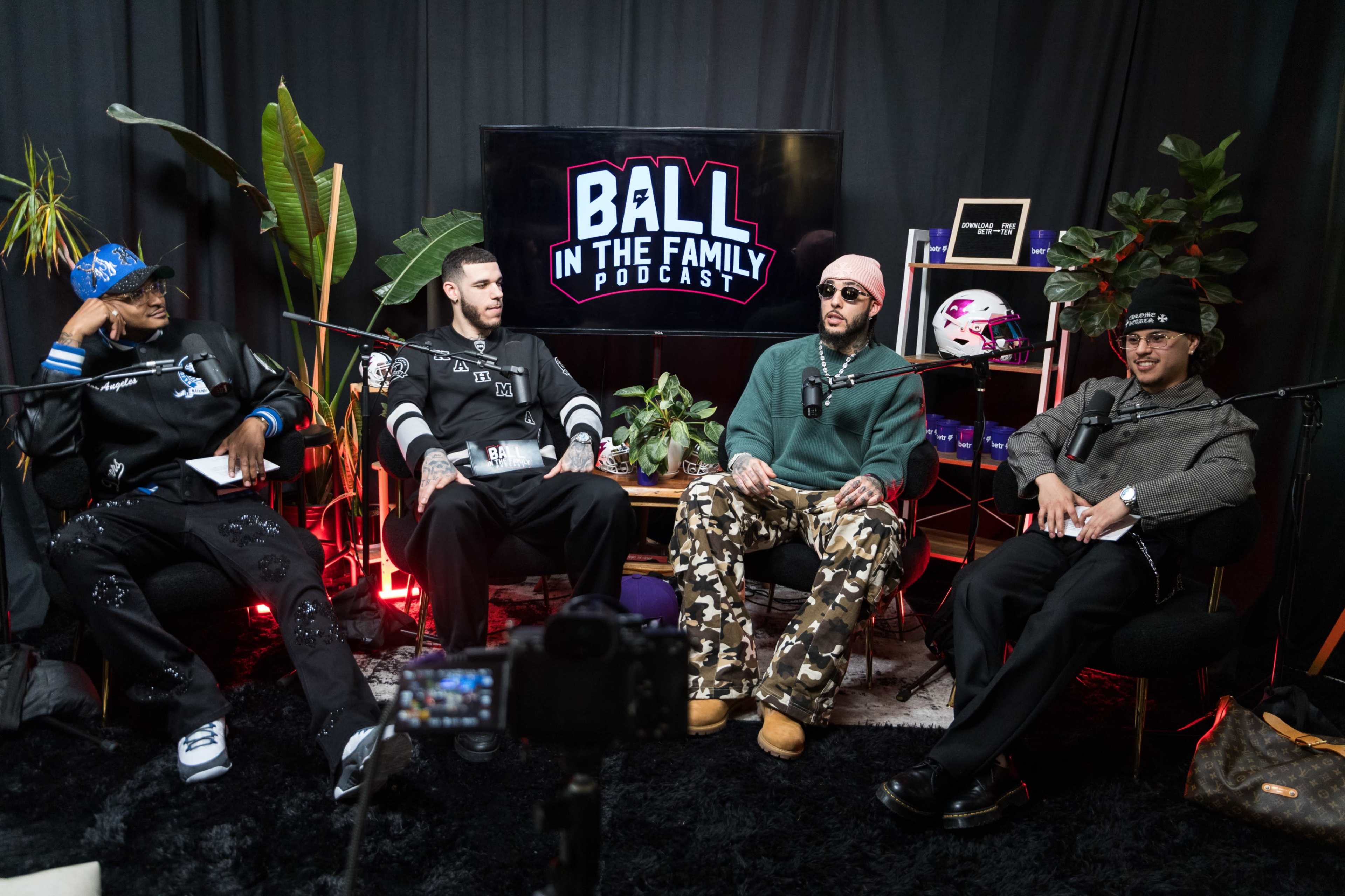 Four men sit in front of a backdrop displaying "BALL IN THE FAMILY PODCAST," surrounded by plants and studio equipment.