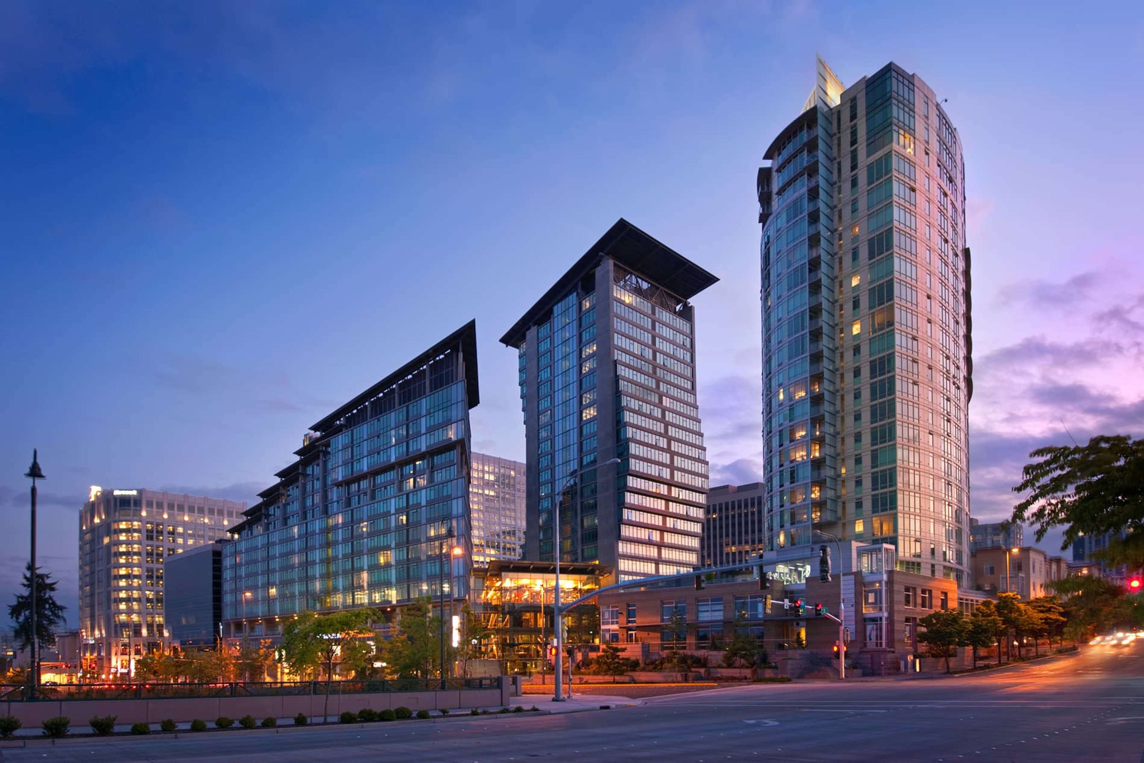 A modern urban skyline featuring three high-rise buildings illuminated during twilight.
