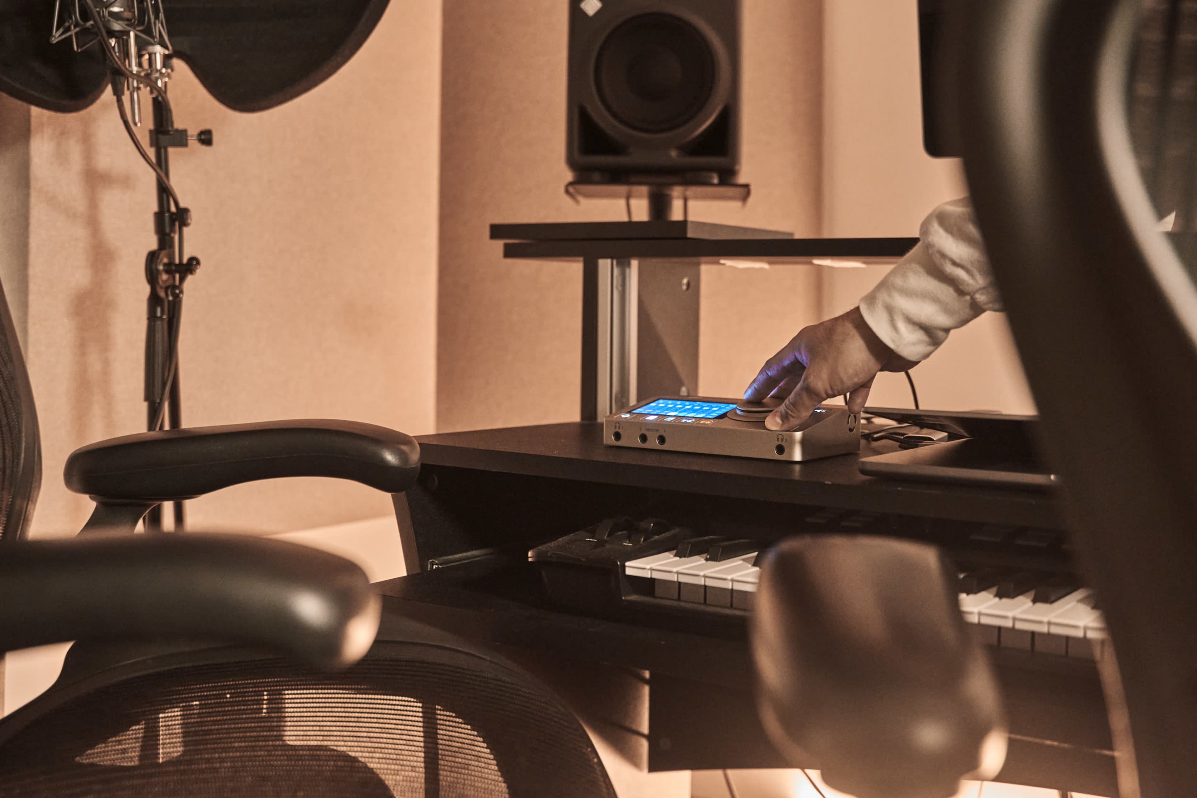 A hand is adjusting a device on a music production desk with a keyboard and studio monitors in a recording studio.