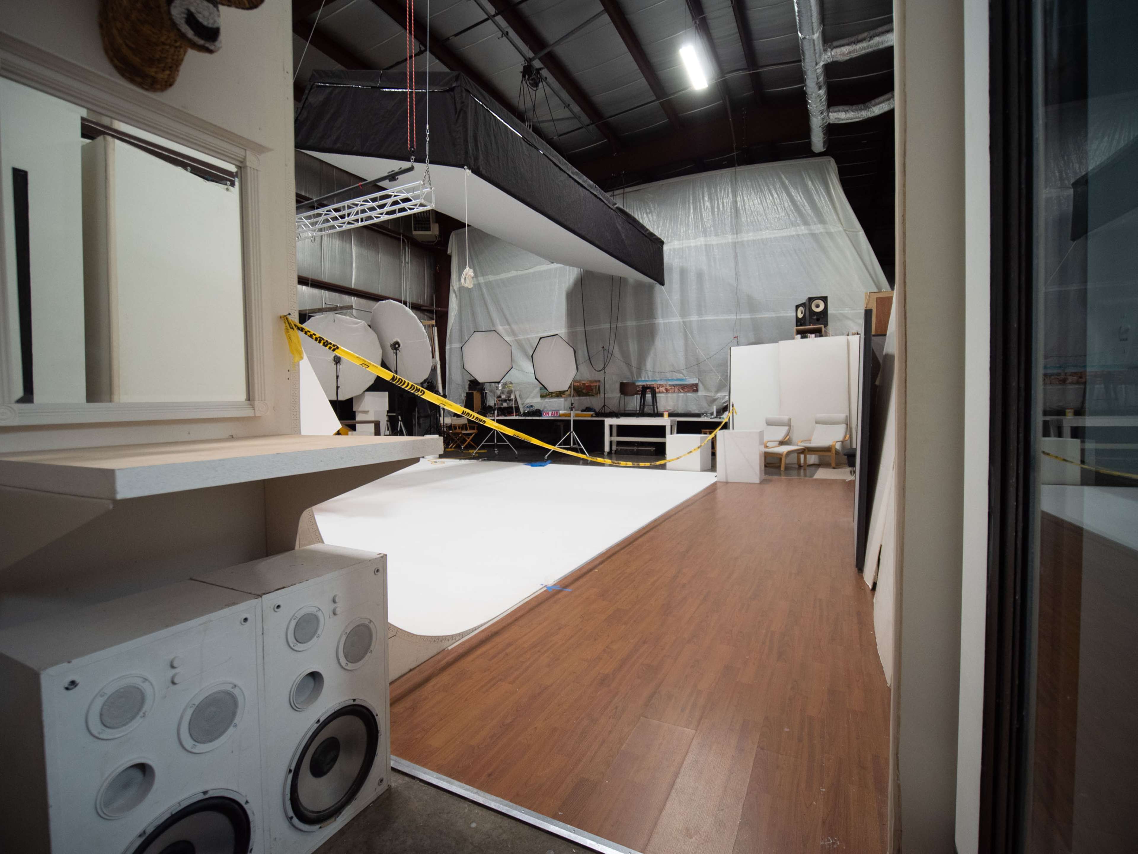 A photography studio featuring a white backdrop, wooden flooring, and various photography equipment in the background.