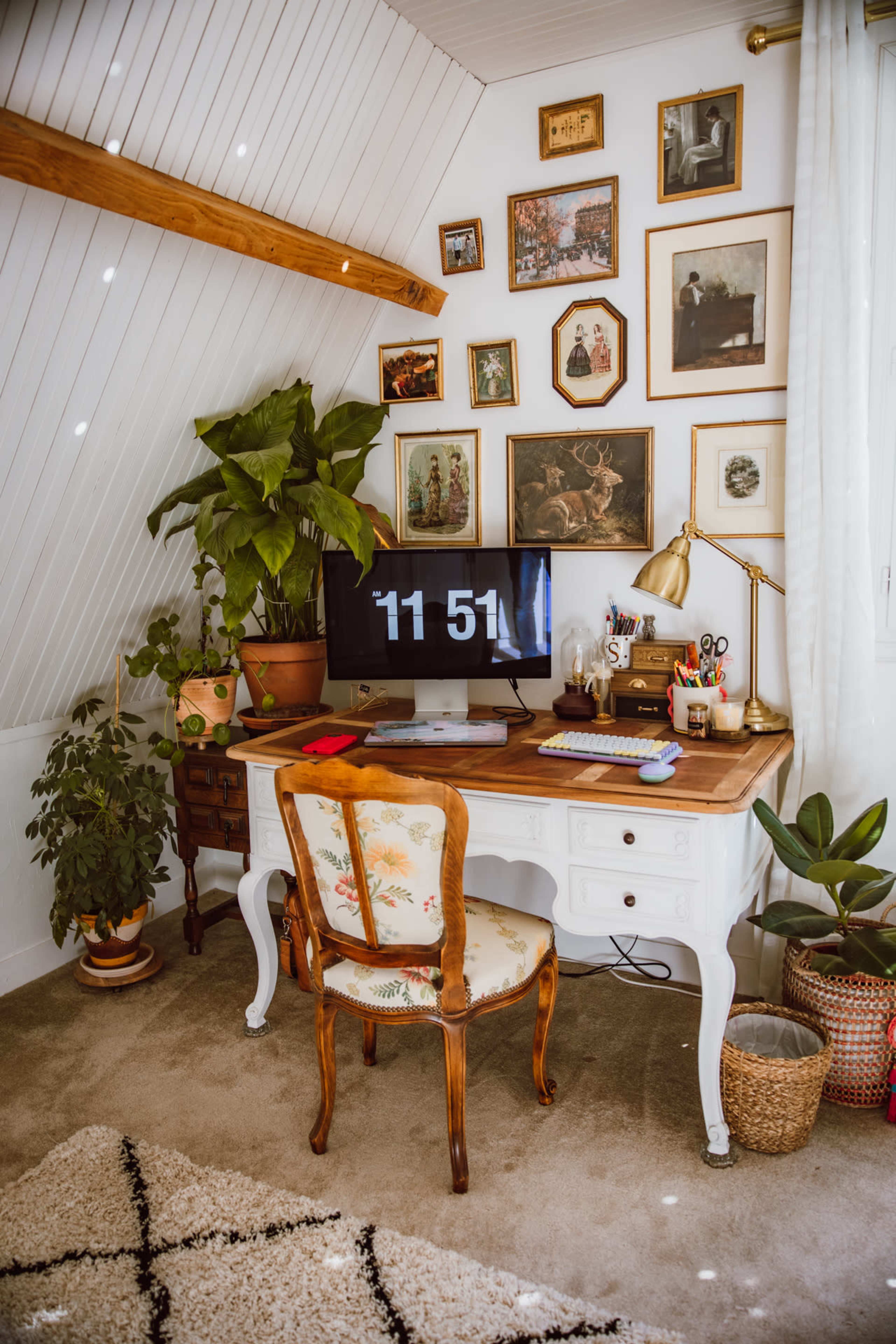 The image shows a neatly organized desk with a computer displaying the time, surrounded by plants and framed pictures on the walls.