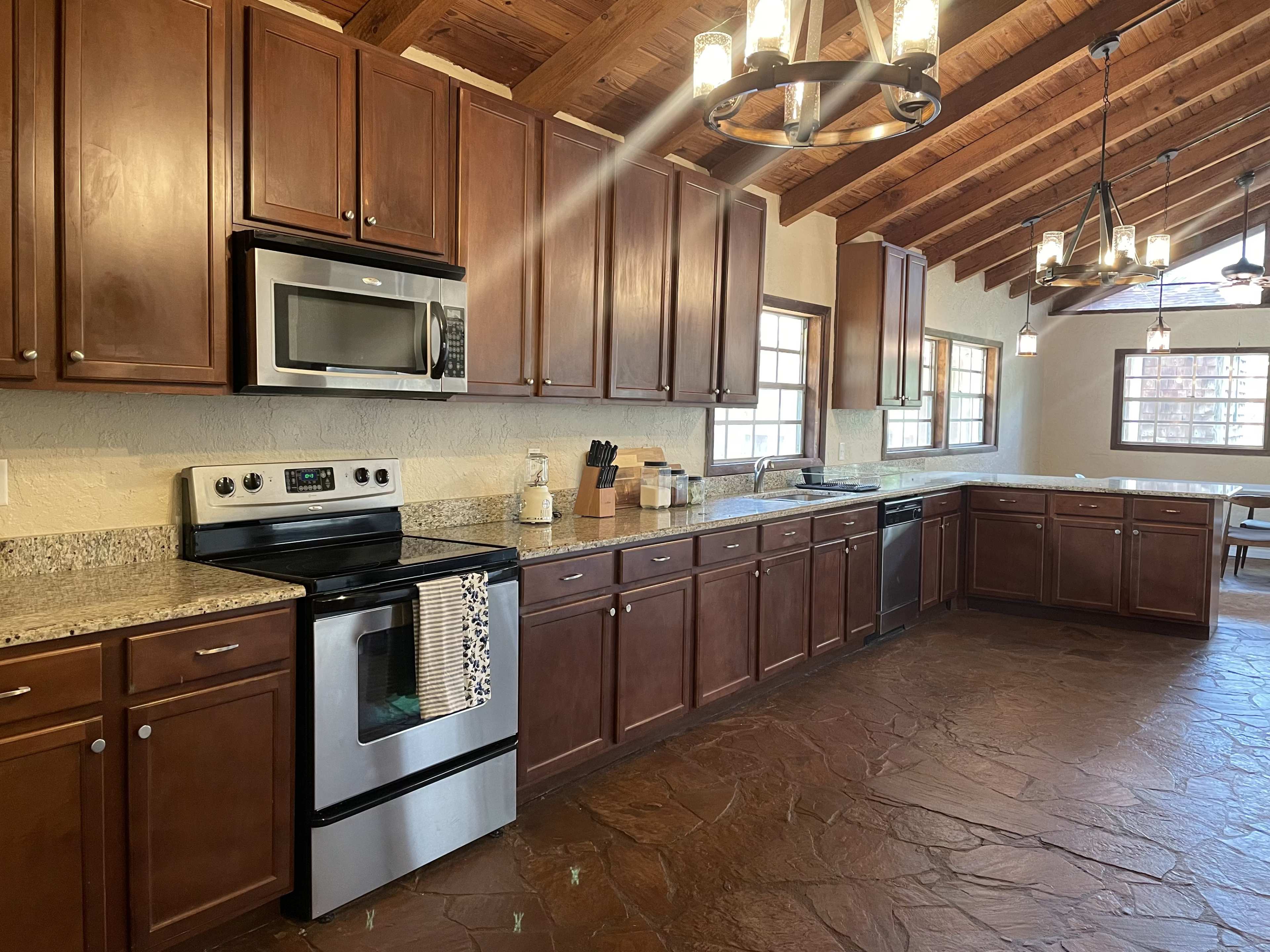 A modern kitchen with wooden cabinets, stainless steel appliances, and a high ceiling featuring exposed beams.