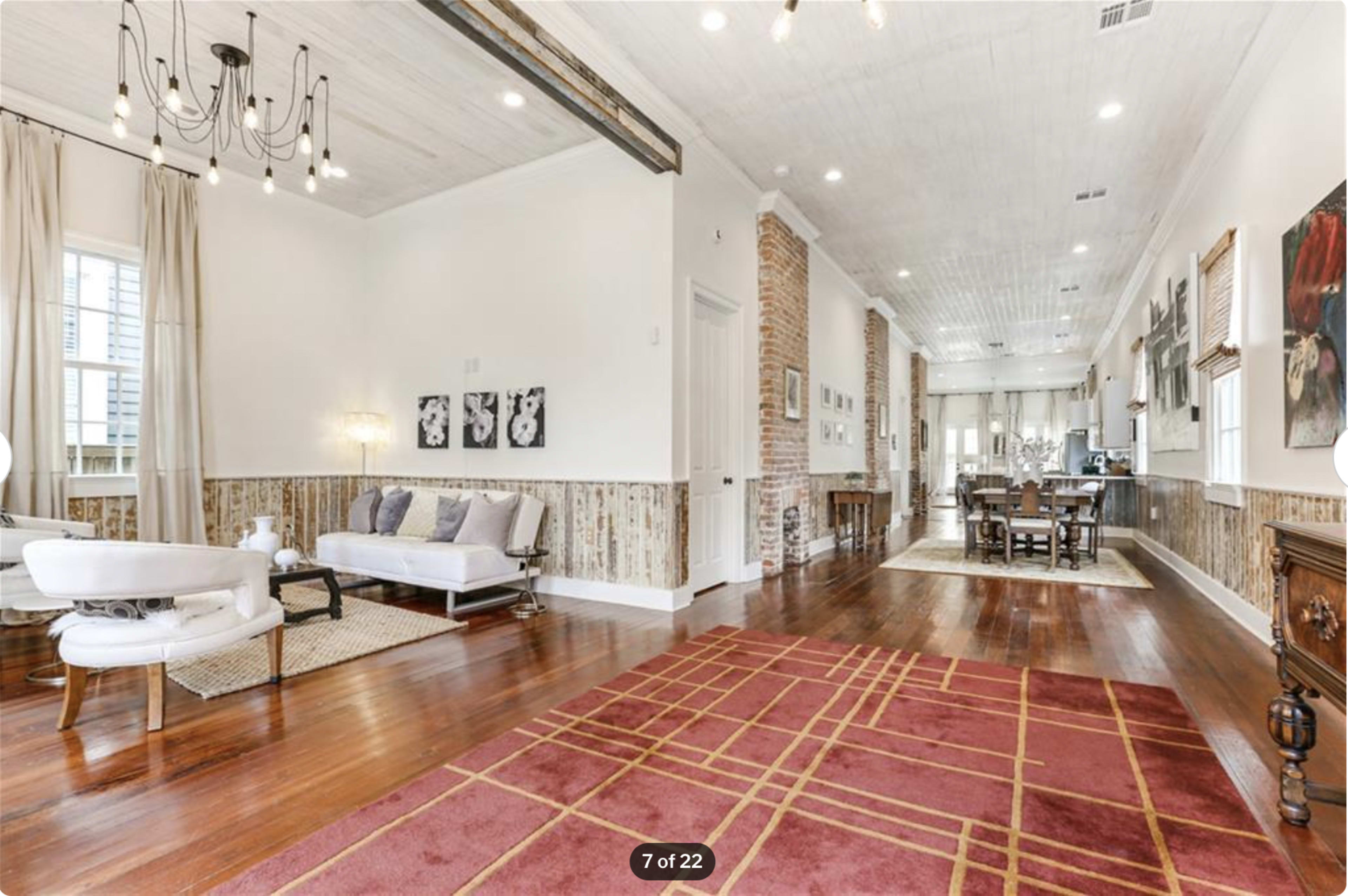 A spacious living area with wooden flooring, a white sofa, and a dining space visible in the background.