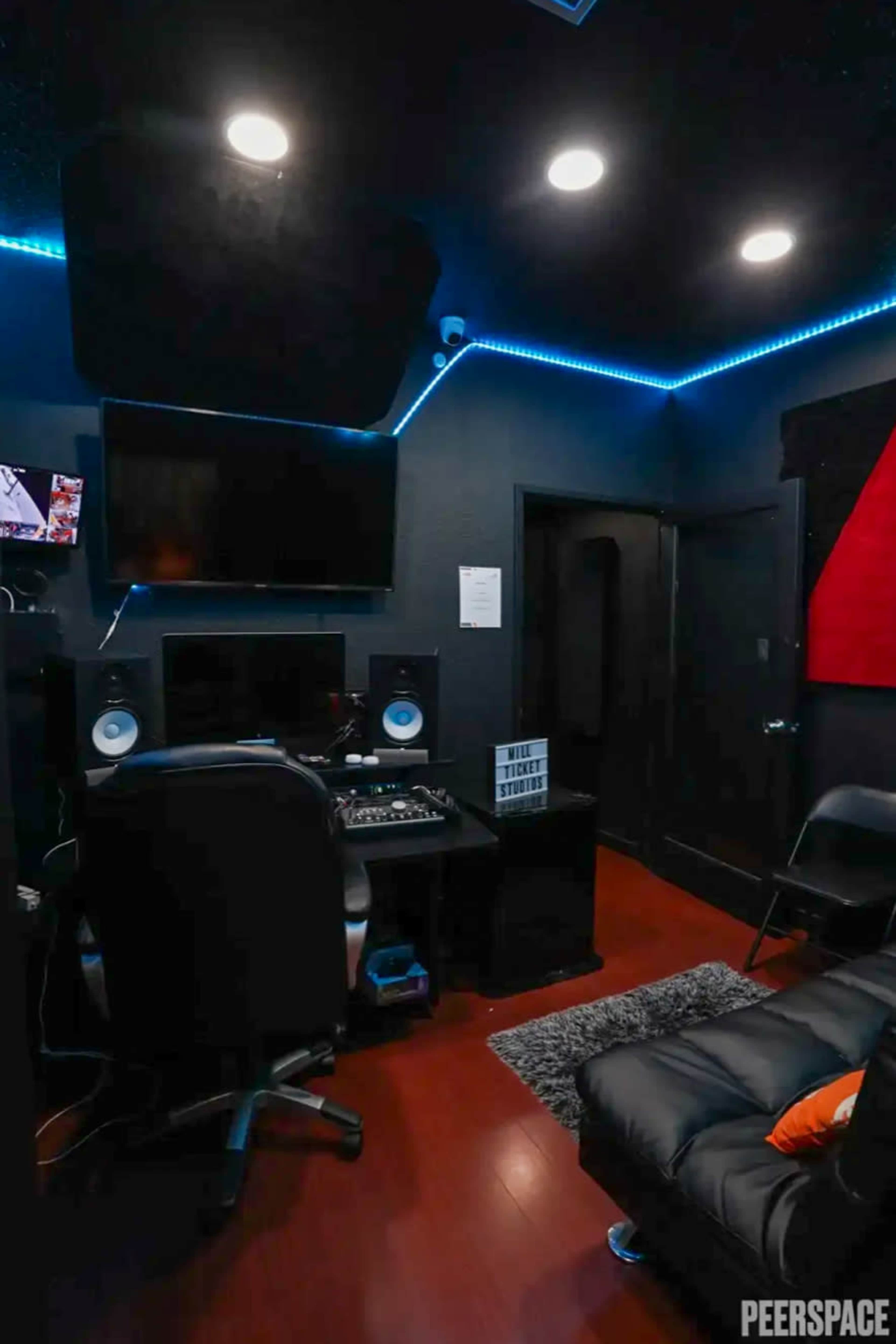 The image shows a dark recording studio with a desk equipped with audio equipment, a computer monitor, and a comfortable couch.